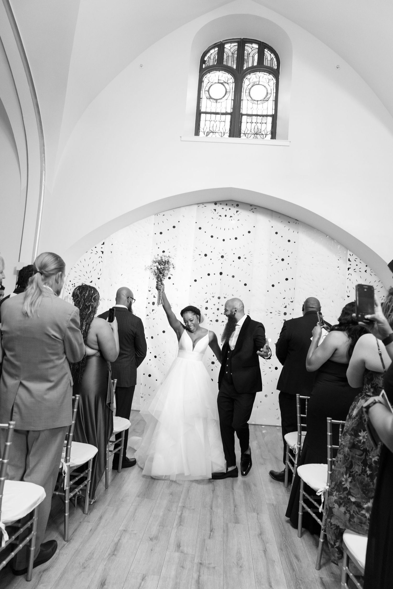 Black and white photo of newlyweds celebrating as they walk down the aisle at their wedding ceremony.