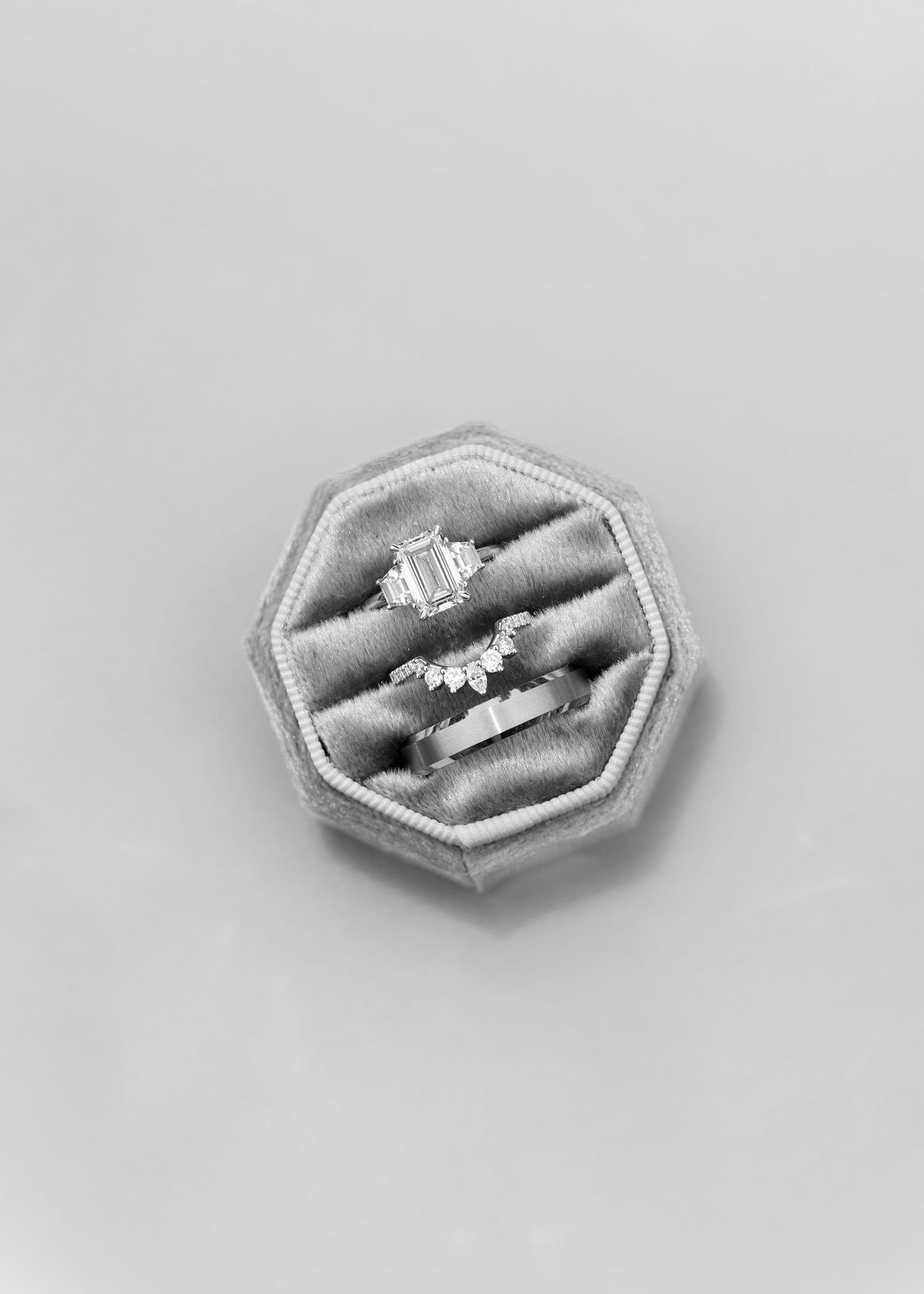 Three diamond wedding rings displayed in an octagonal velvet ring box in black and white photo.