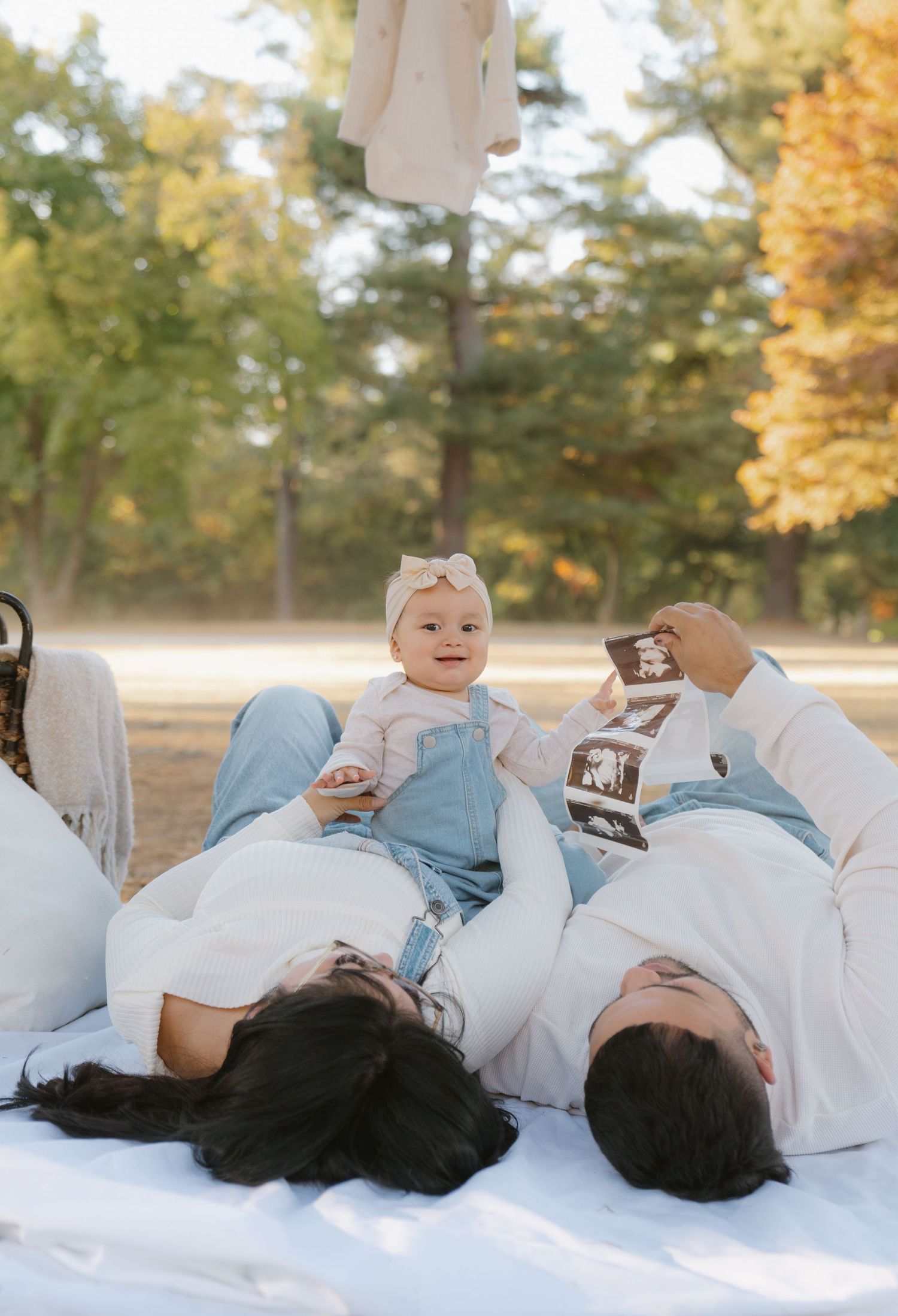 A series of four connected photos showing people lying on a white blanket outdoors during autumn with trees in background.