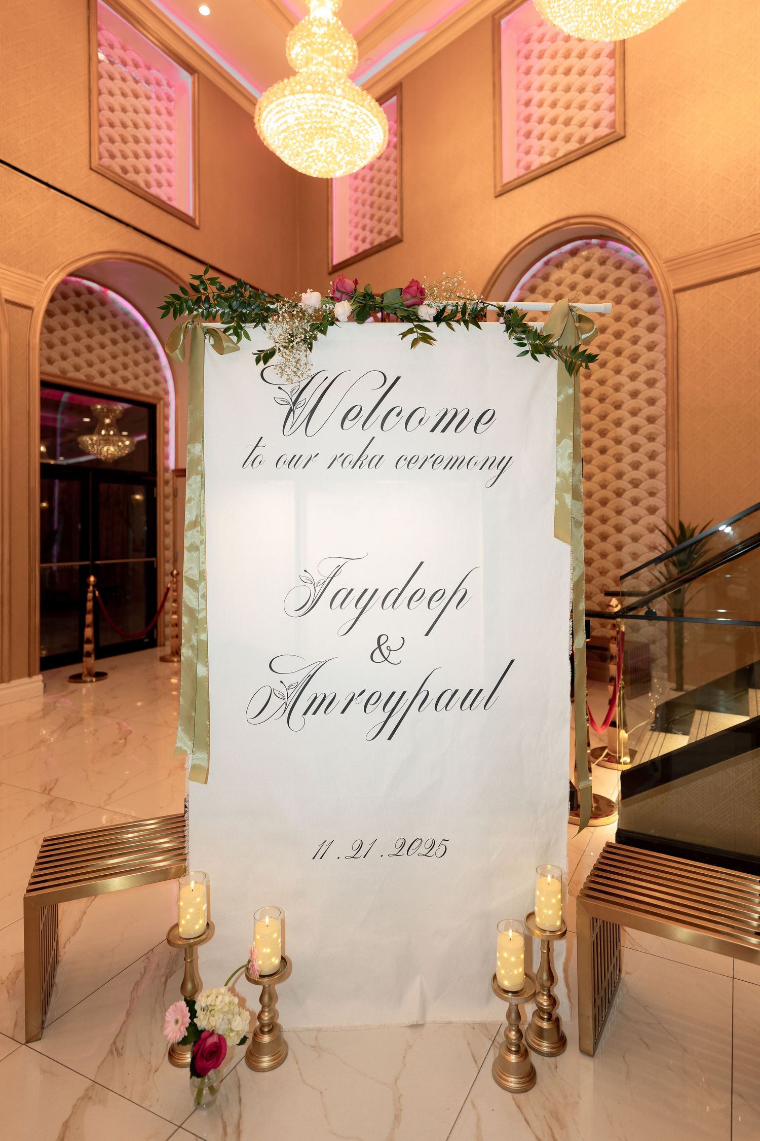 Elegant wedding welcome sign with floral decorations and crystal chandeliers in a luxurious venue entrance.