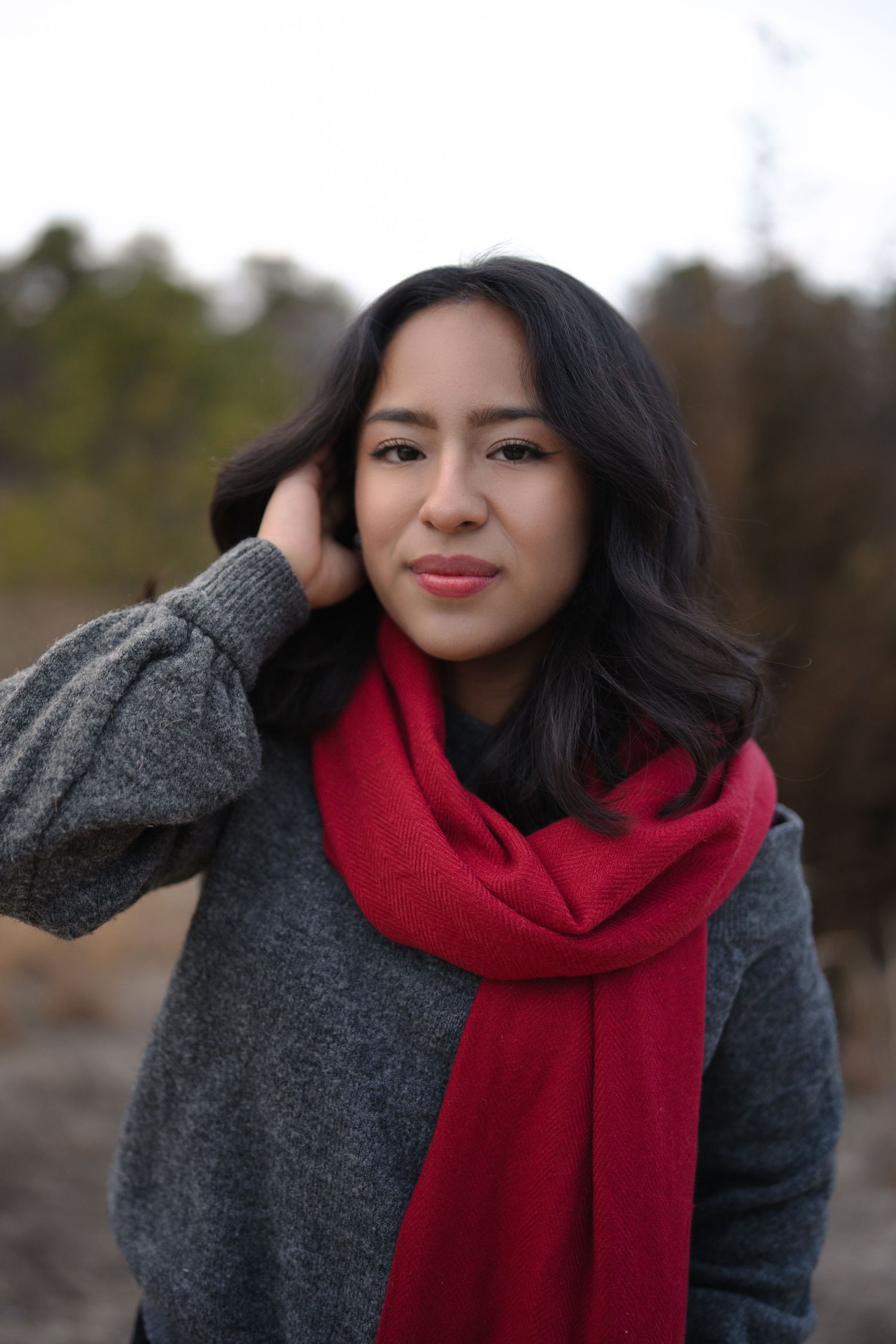 Winter portrait featuring grey sweater and bright red scarf outdoors.