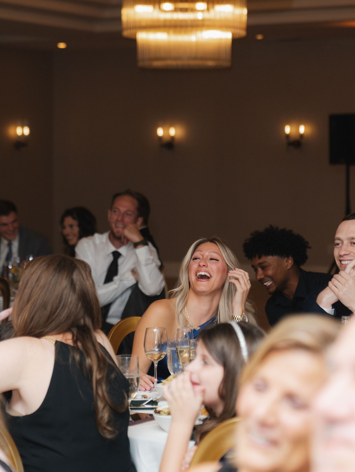 A group of people laughing and enjoying themselves at a dimly lit formal event with warm lighting and elegant decor.