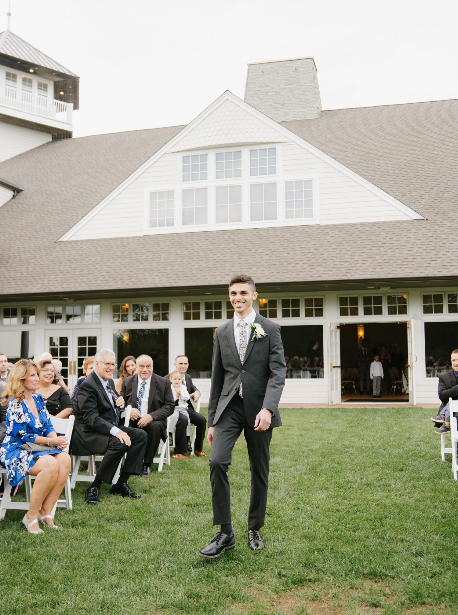 Wedding party members play lawn games during an outdoor reception at an elegant white venue with a grassy area.