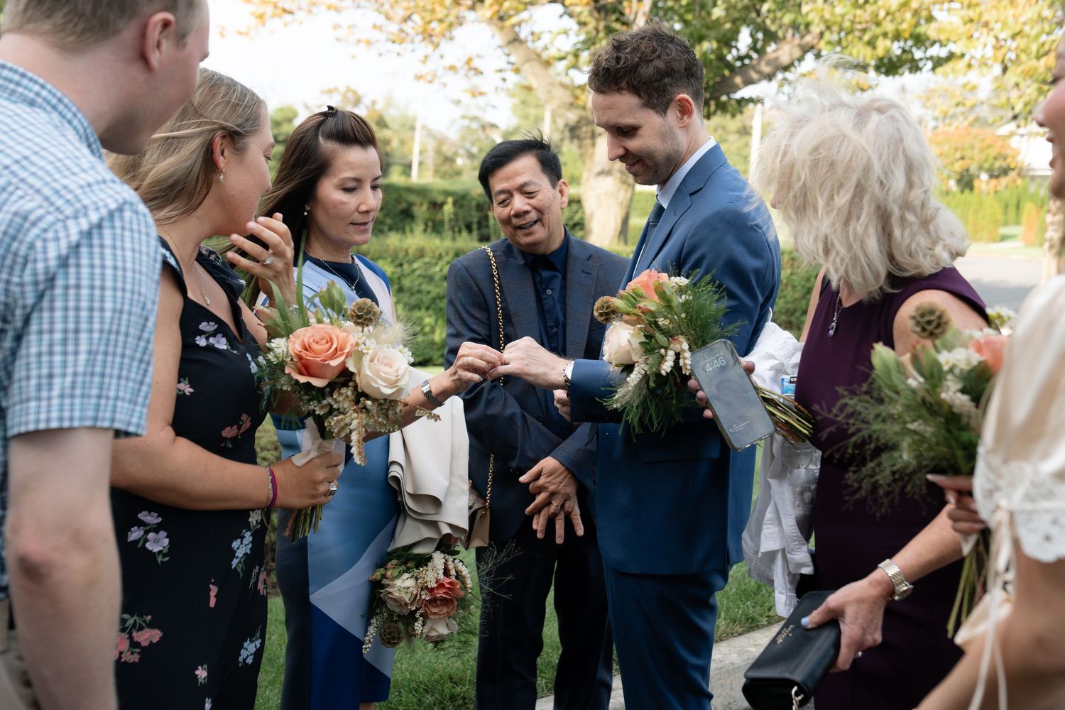 Wedding party members gather outdoors in casual conversation during autumn.