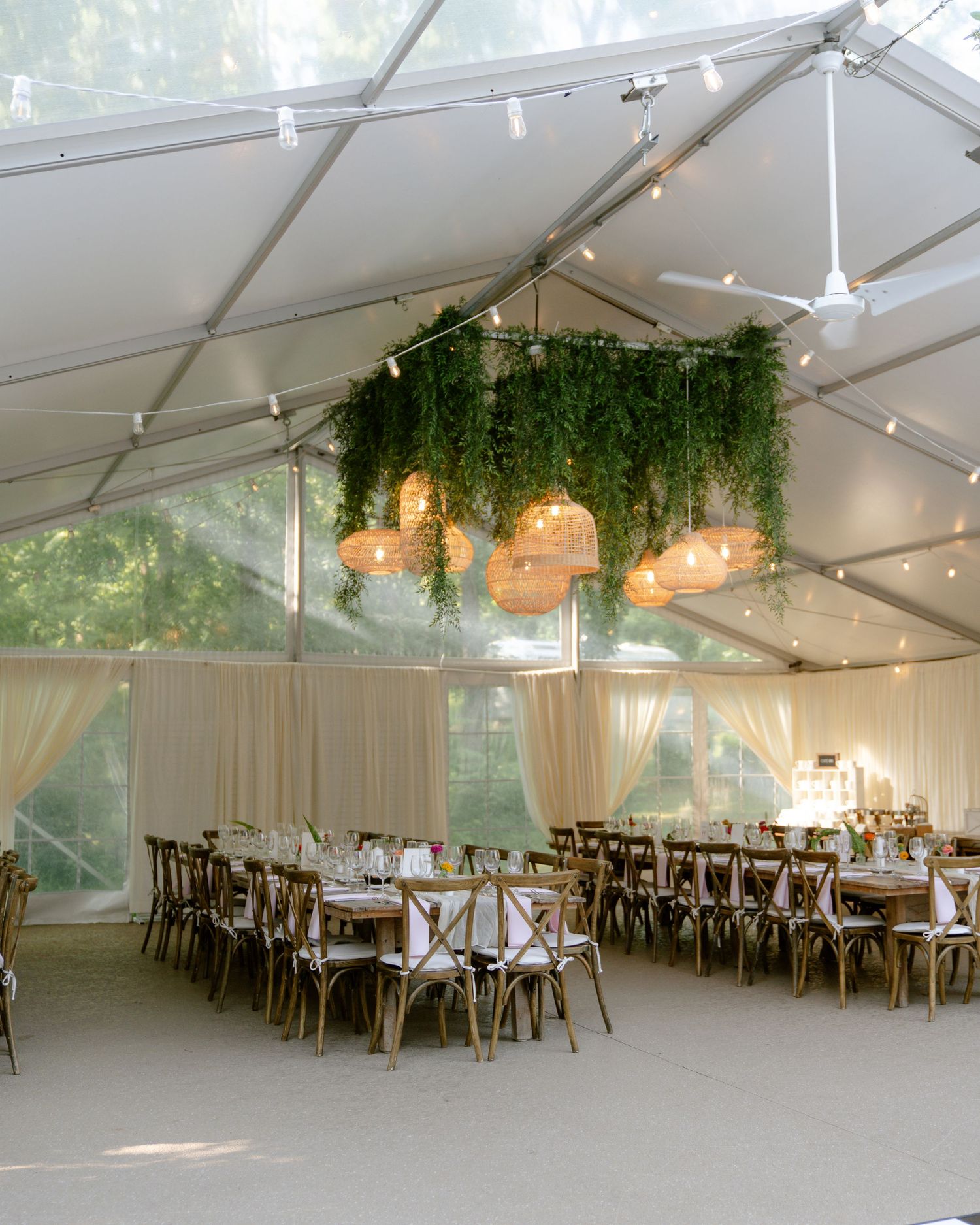 Elegant wedding reception tent setup with hanging greenery and string lights.