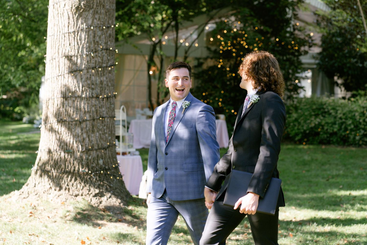 Wedding guests gathered under tall trees during an outdoor celebration.