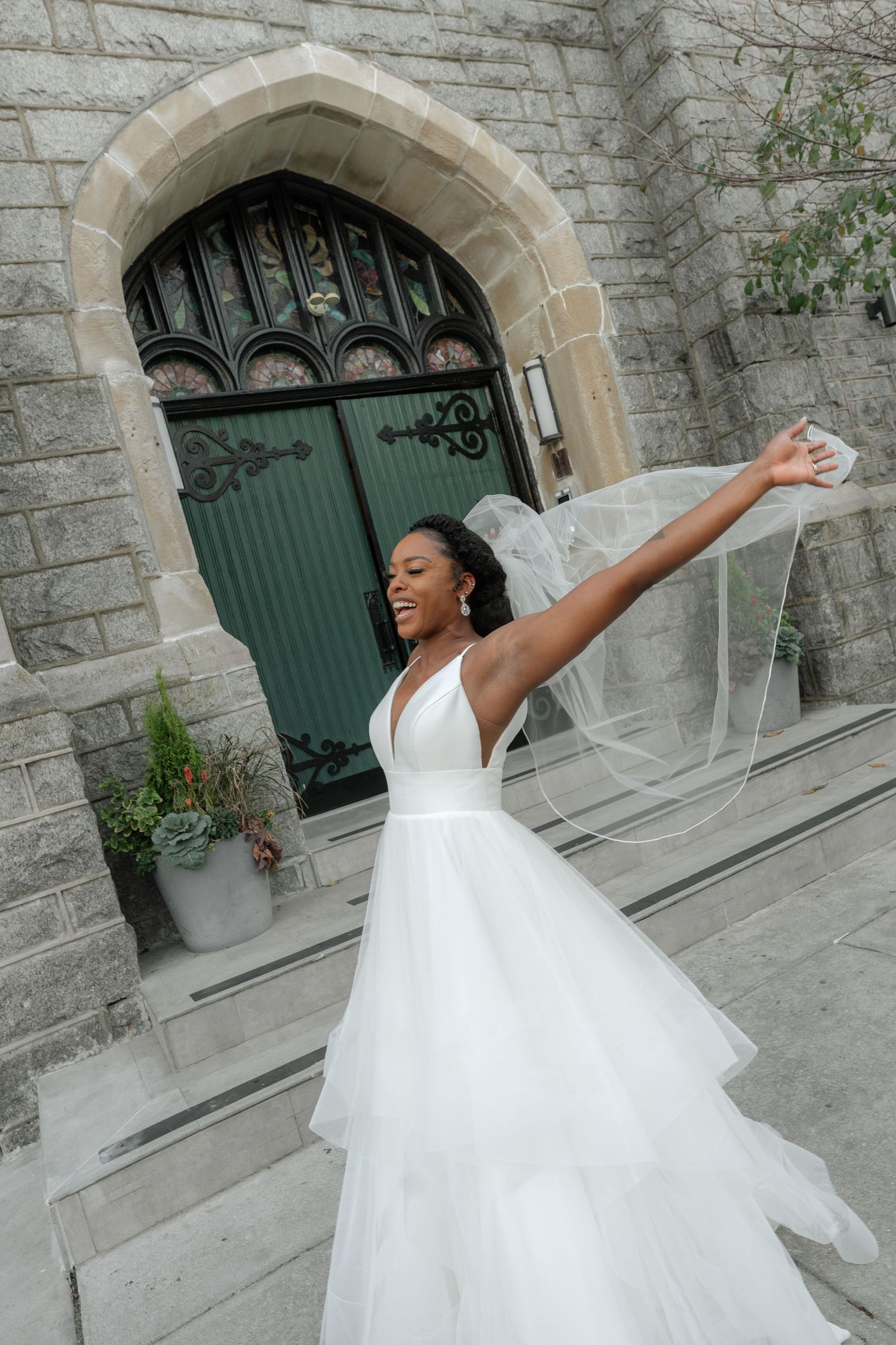 A joyful bride twirls in her flowing white wedding gown outside a stone church.