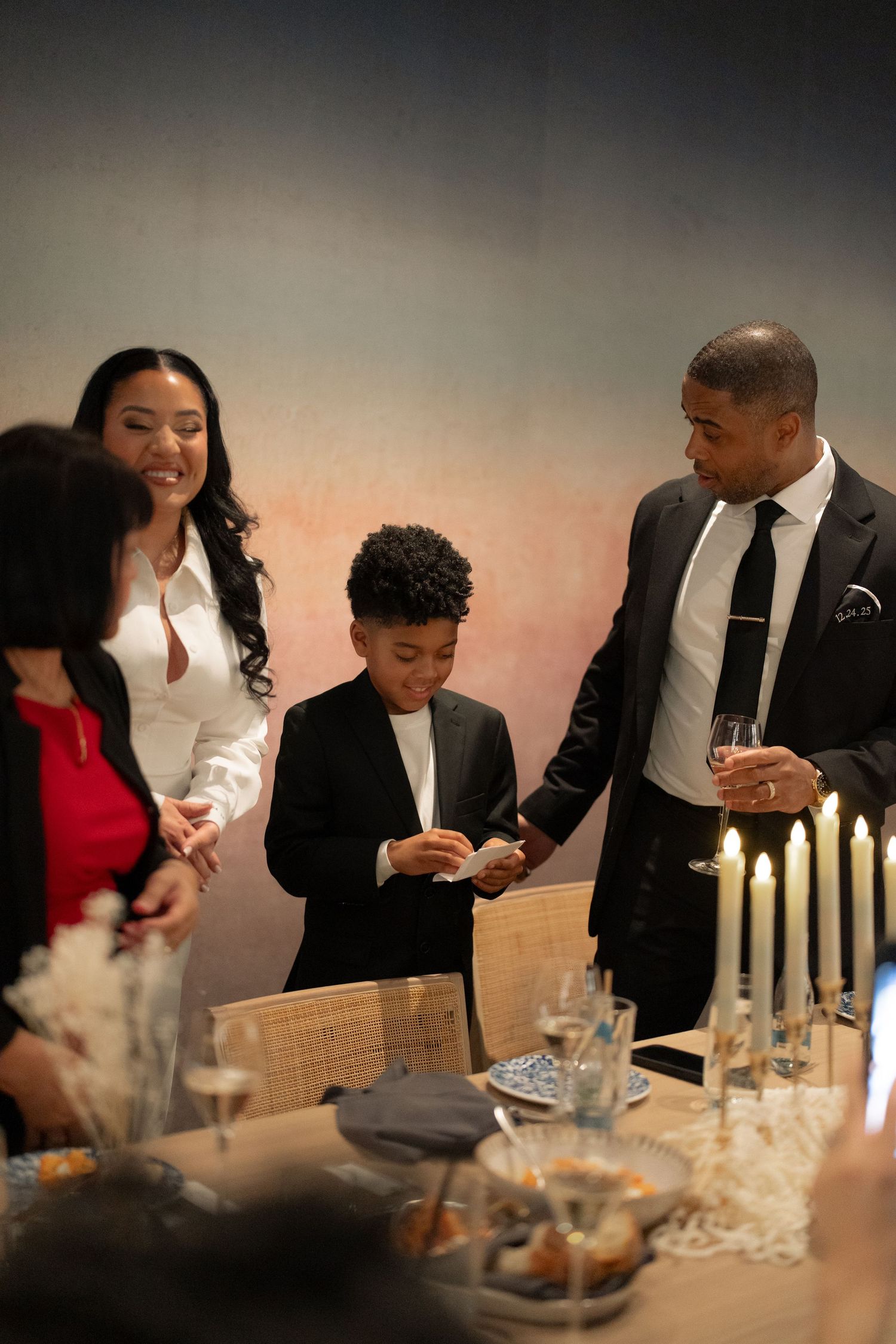Elegant dinner party scene with lit candles and guests seated at a formal table setting.