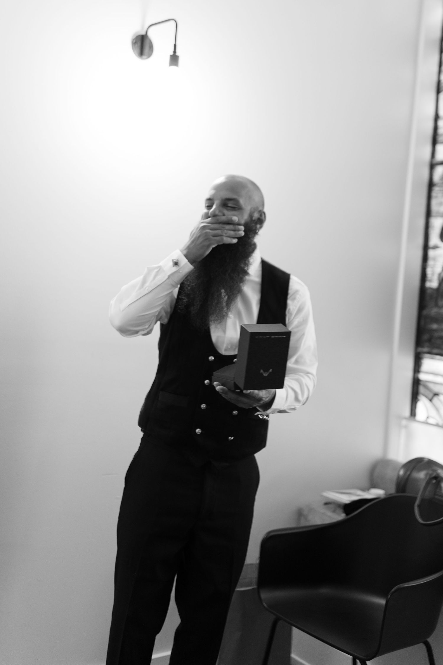 Black and white photo of a person in formal vest and shirt holding something to their face.
