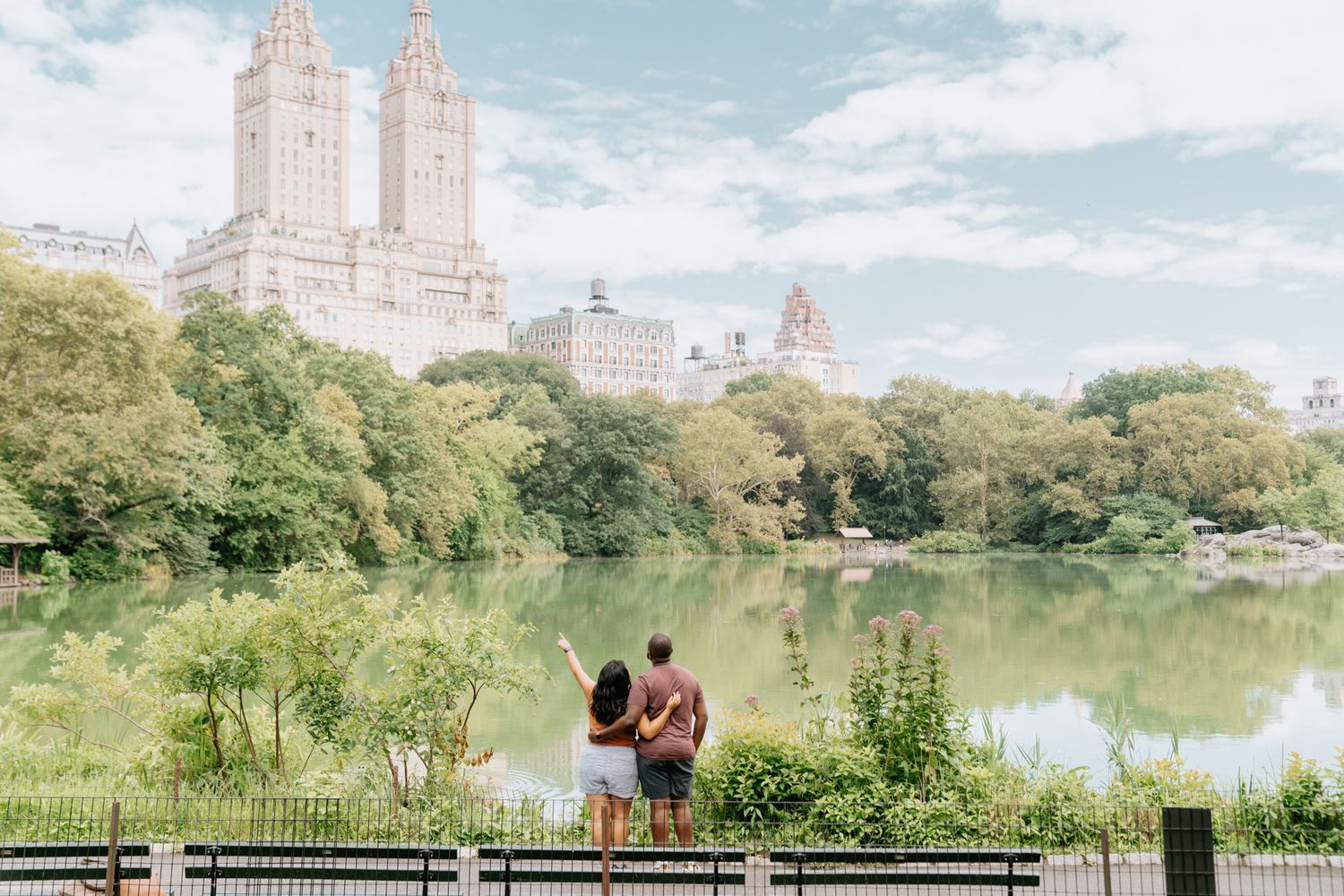 Romantic couple photography session overlooking Central Park lake with city buildings in background.