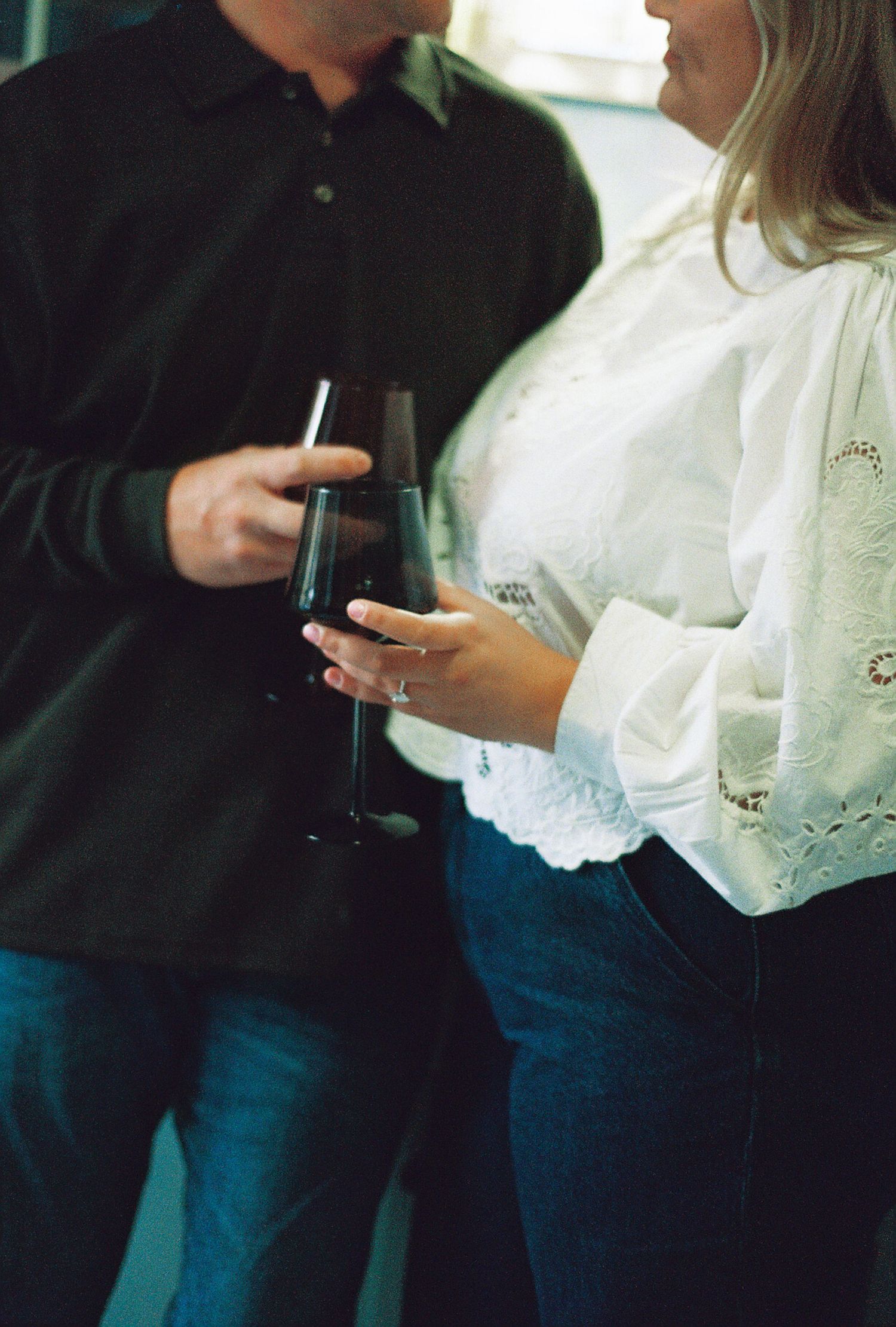 Two people holding wine glasses share an intimate conversation in casual attire.