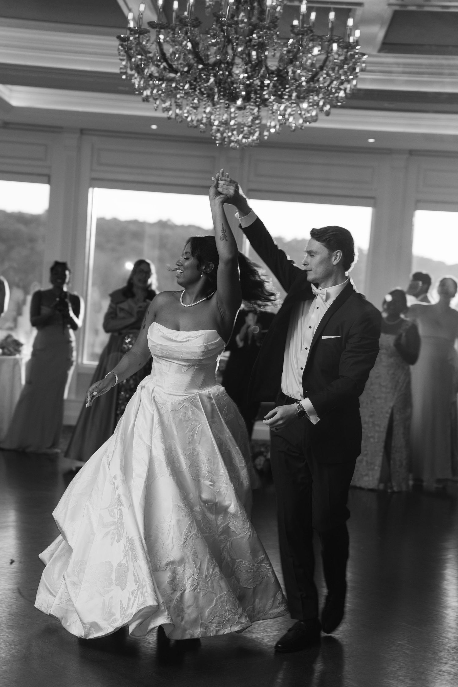 Black and white photo of newlyweds dancing under a chandelier during their first dance.