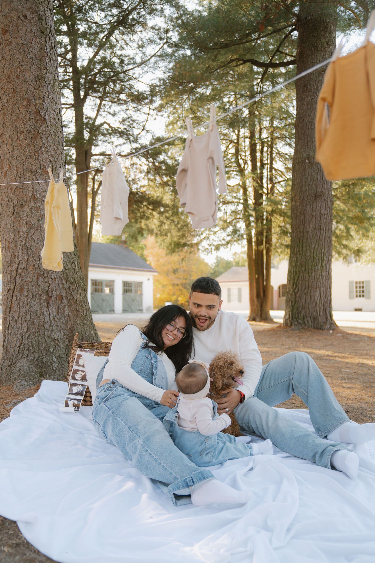 Family and their fluffy goldendoodle dog cuddle together on a white blanket outdoors during a photo session.