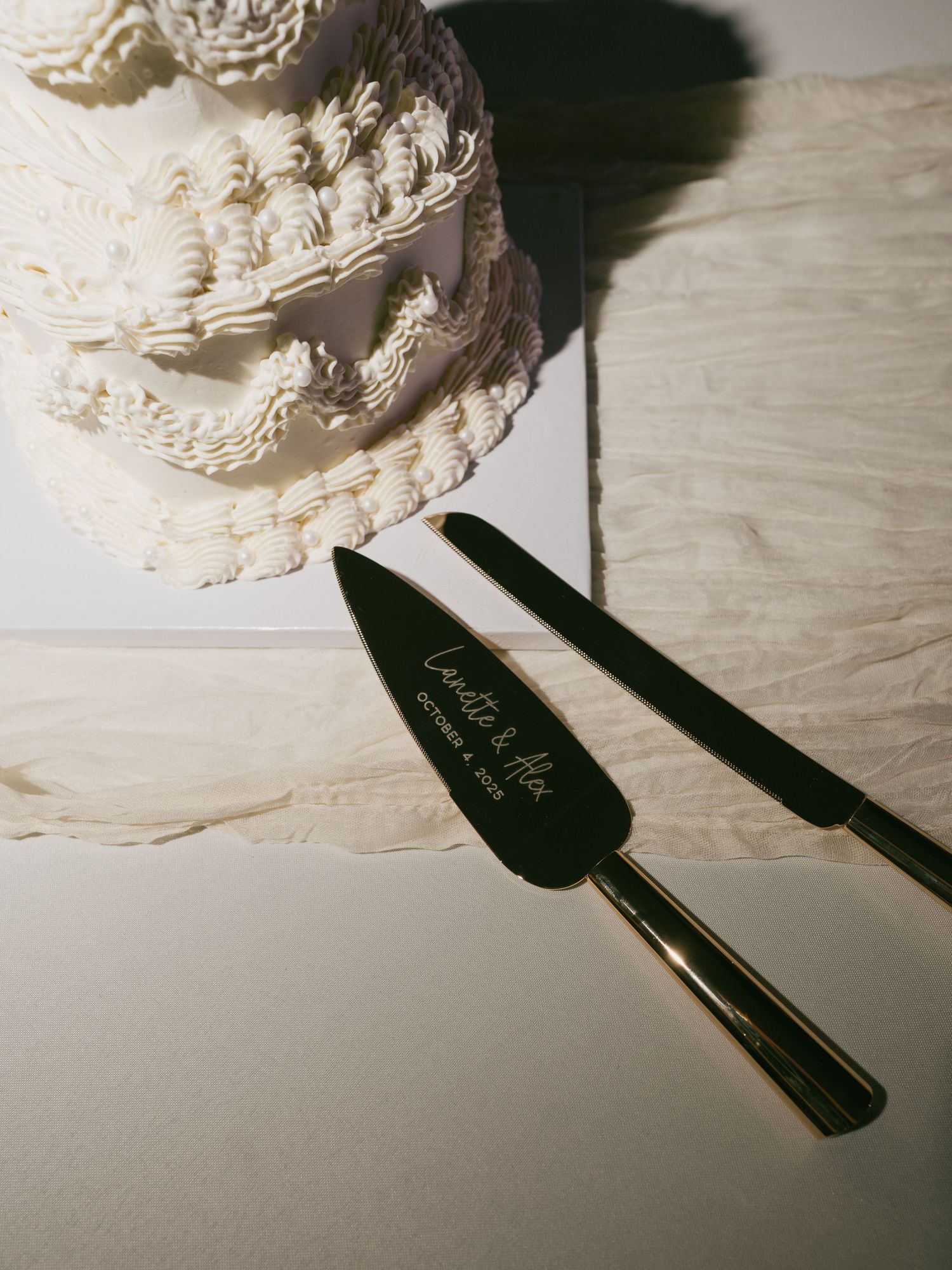Close-up of an elegant white wedding cake being cut with a decorative serving knife.
