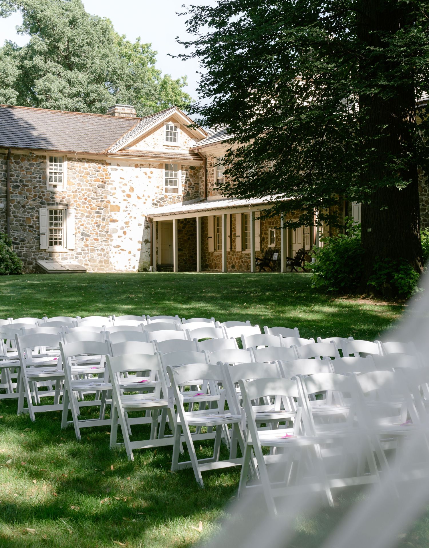Rows of white folding chairs set up on a lawn for an outdoor ceremony in front of a historic stone building.