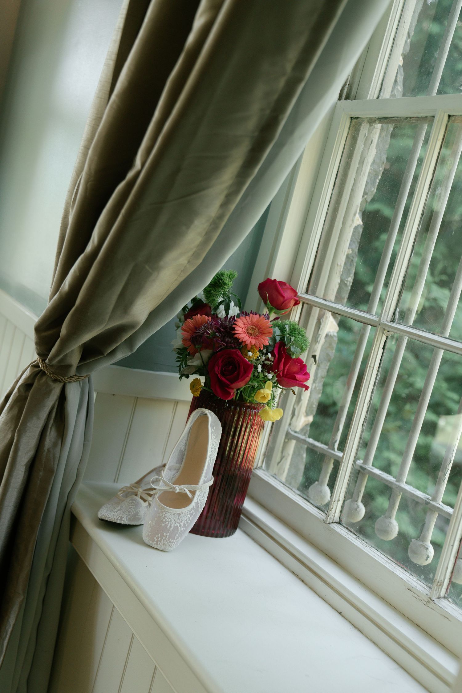 Elegant floral arrangements in vases sit on a windowsill with natural light streaming through white curtains.