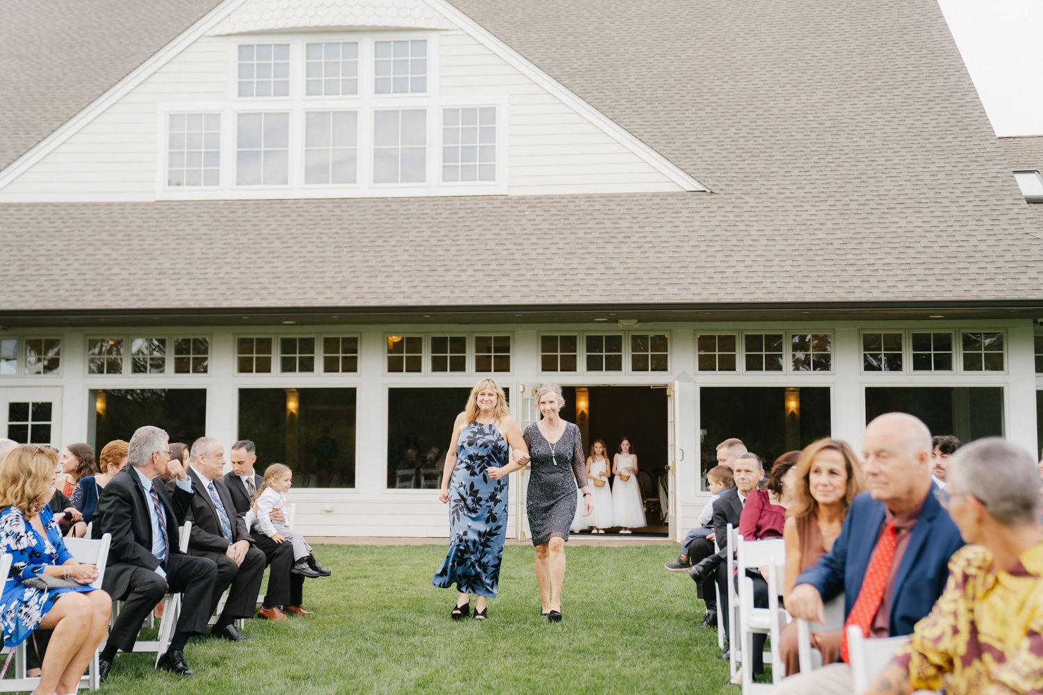Wedding guests gather outside a white building for an outdoor reception celebration.