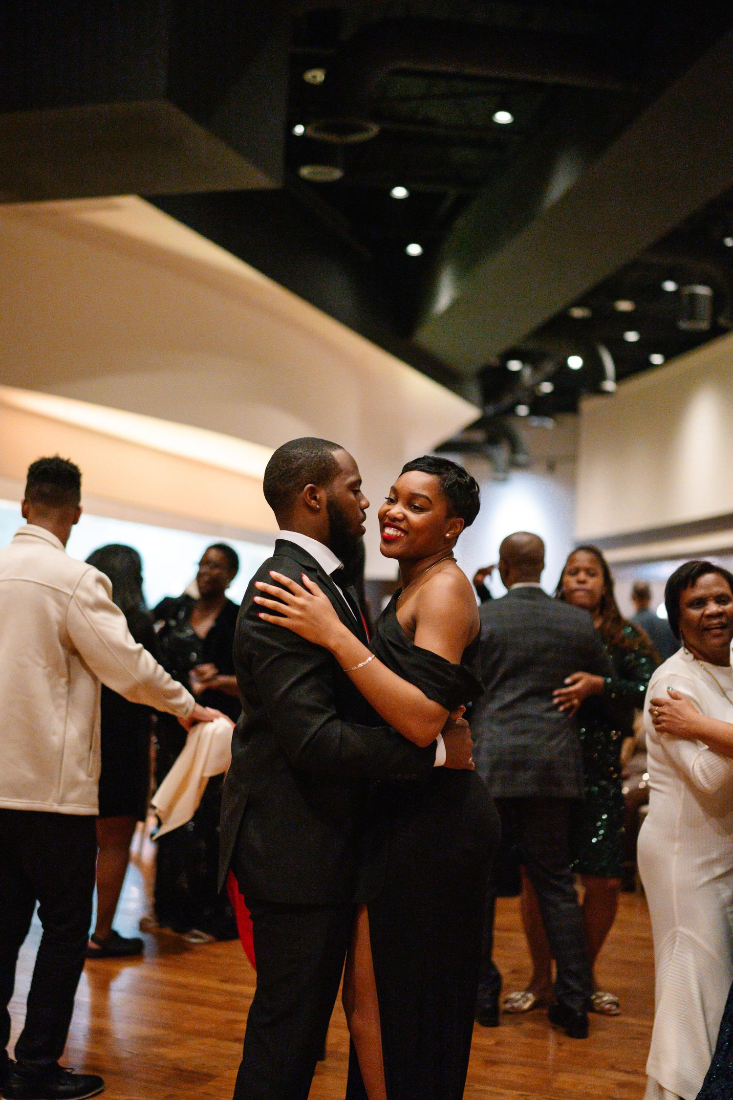 Couple dancing intimately at an indoor reception with other guests in the background.