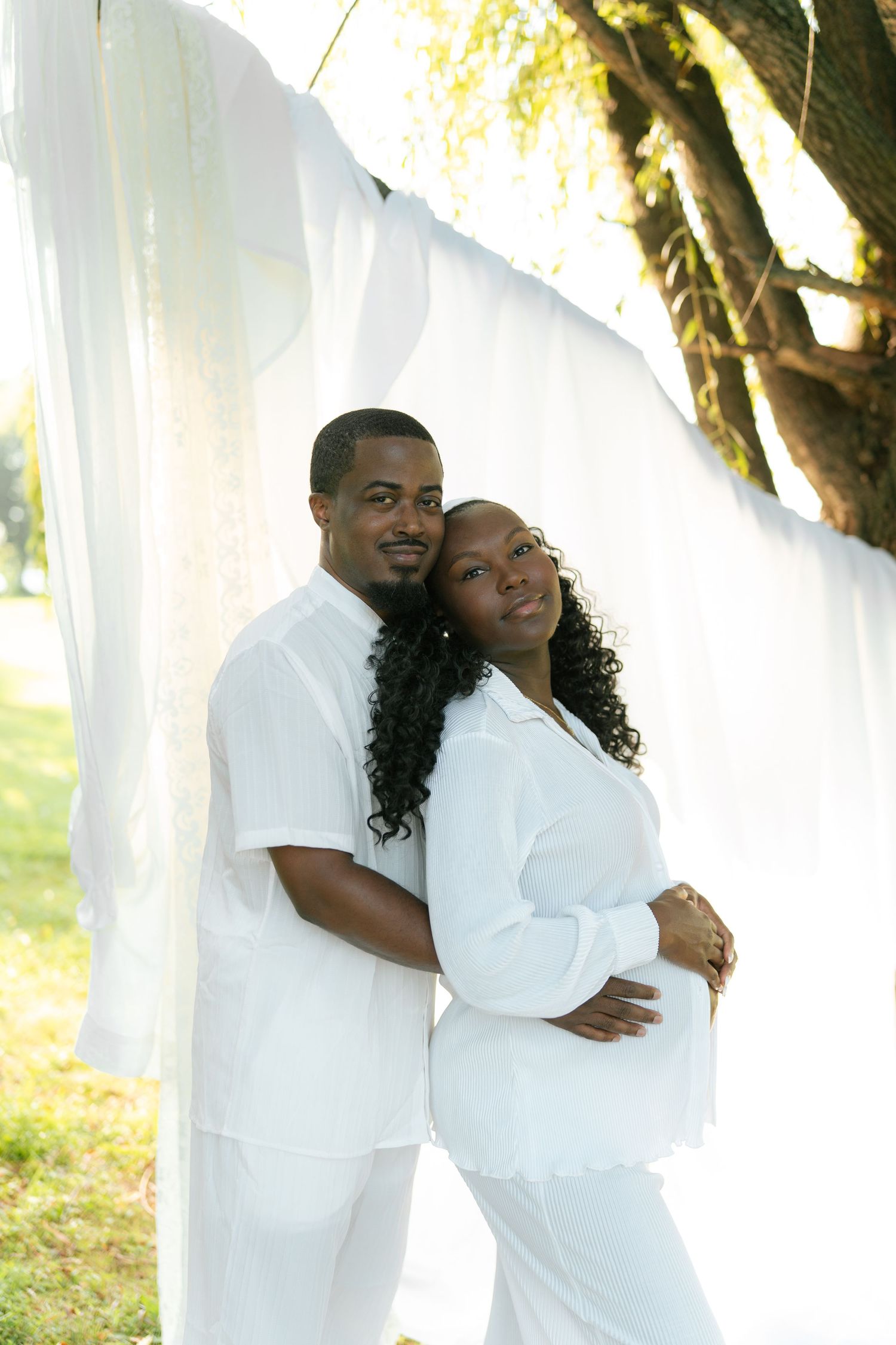 Couple in white outfits embracing outdoors against flowing white fabric backdrop.