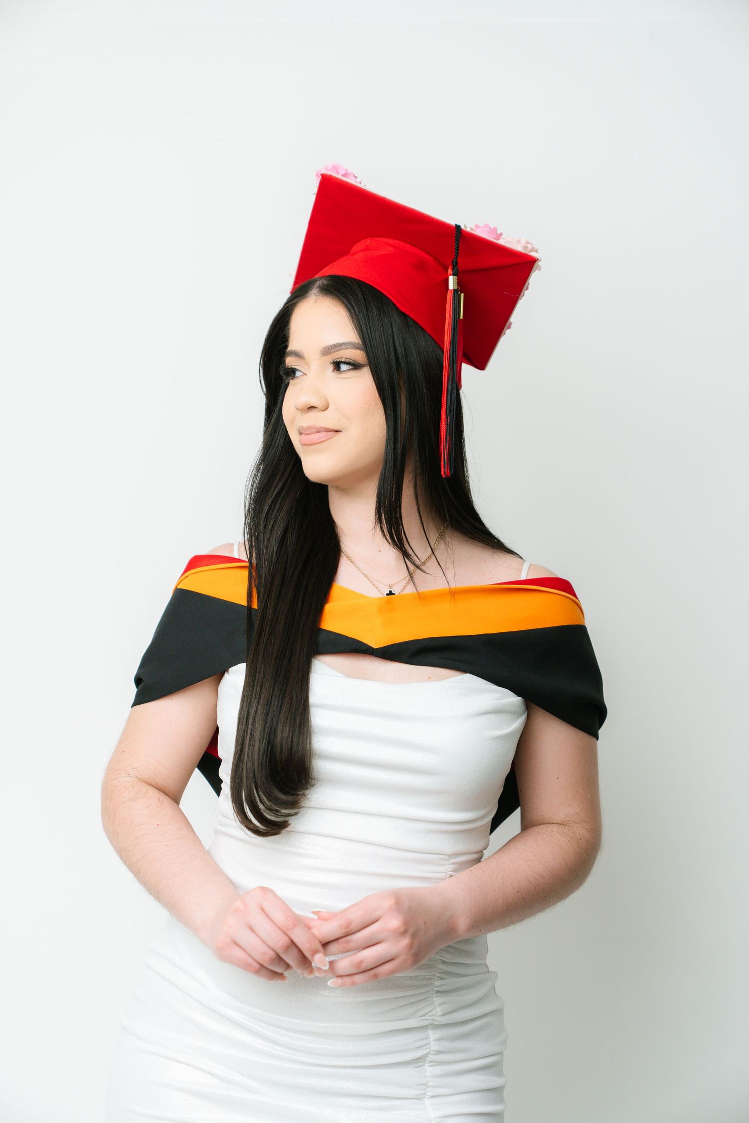 Graduate in red cap and white graduation gown against white background.