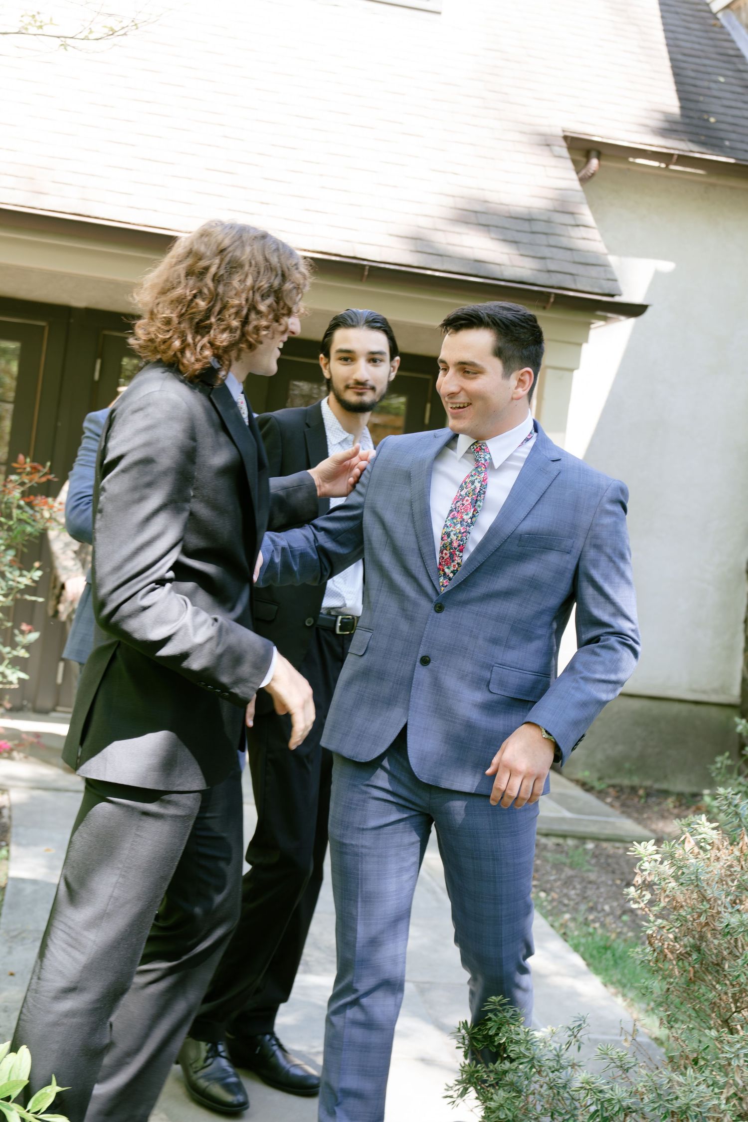 Groomsmen in suits sharing laughs and embracing during pre-wedding preparations.