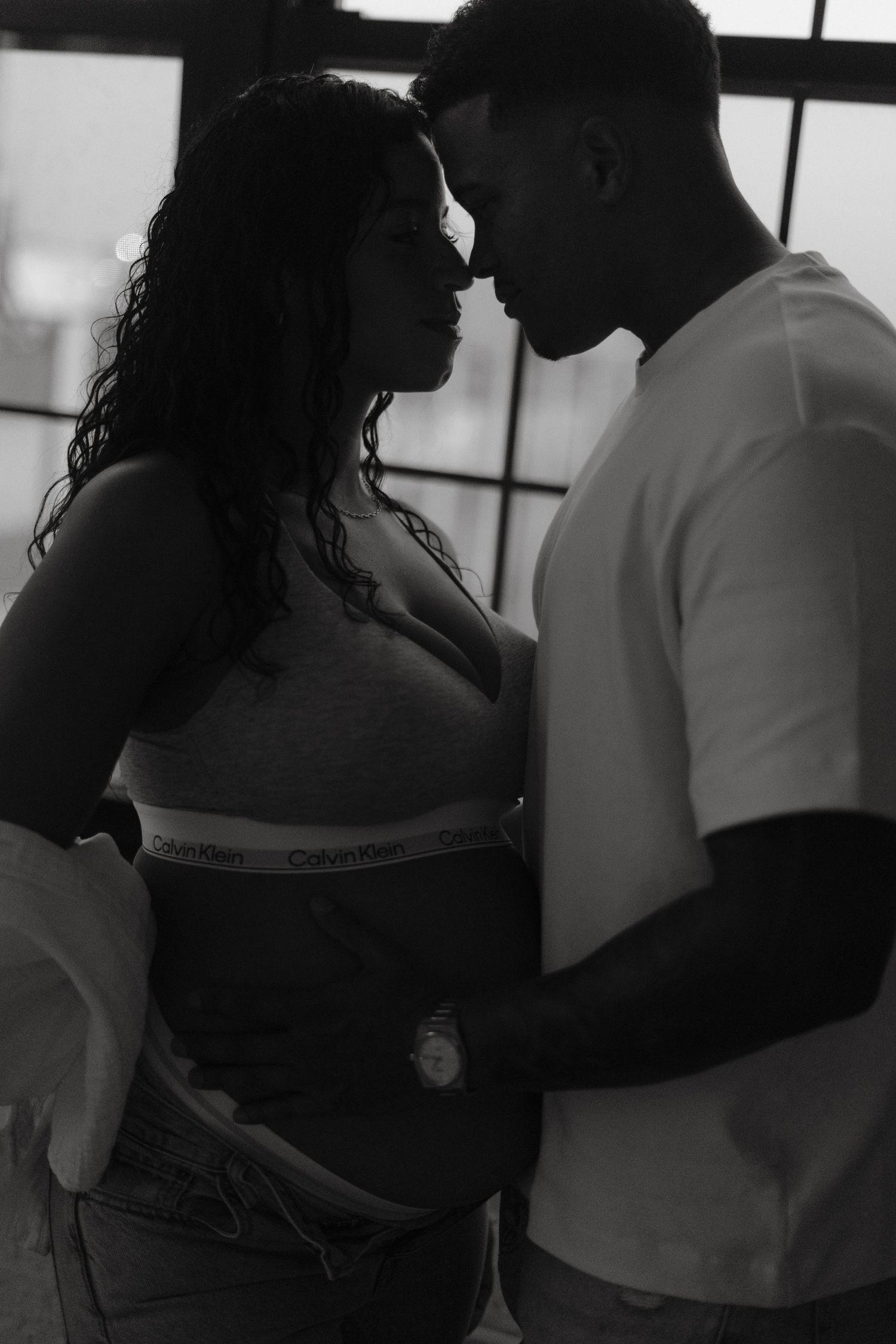 Black and white silhouette of a romantic couple facing each other intimately near a large window.