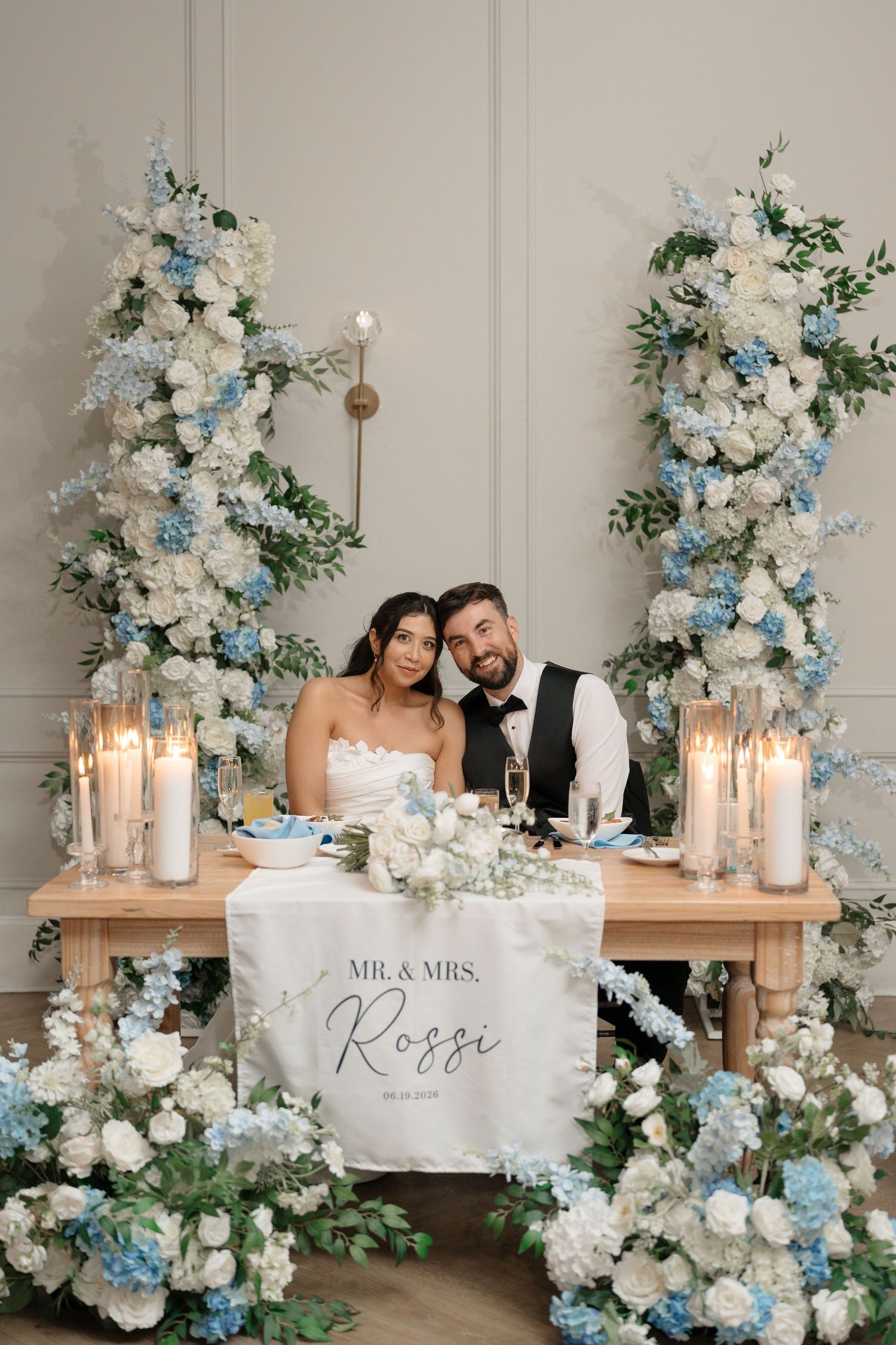 Mr. & Mrs. Rossi sit at a sweetheart table adorned with blue and white floral arrangements and candles.