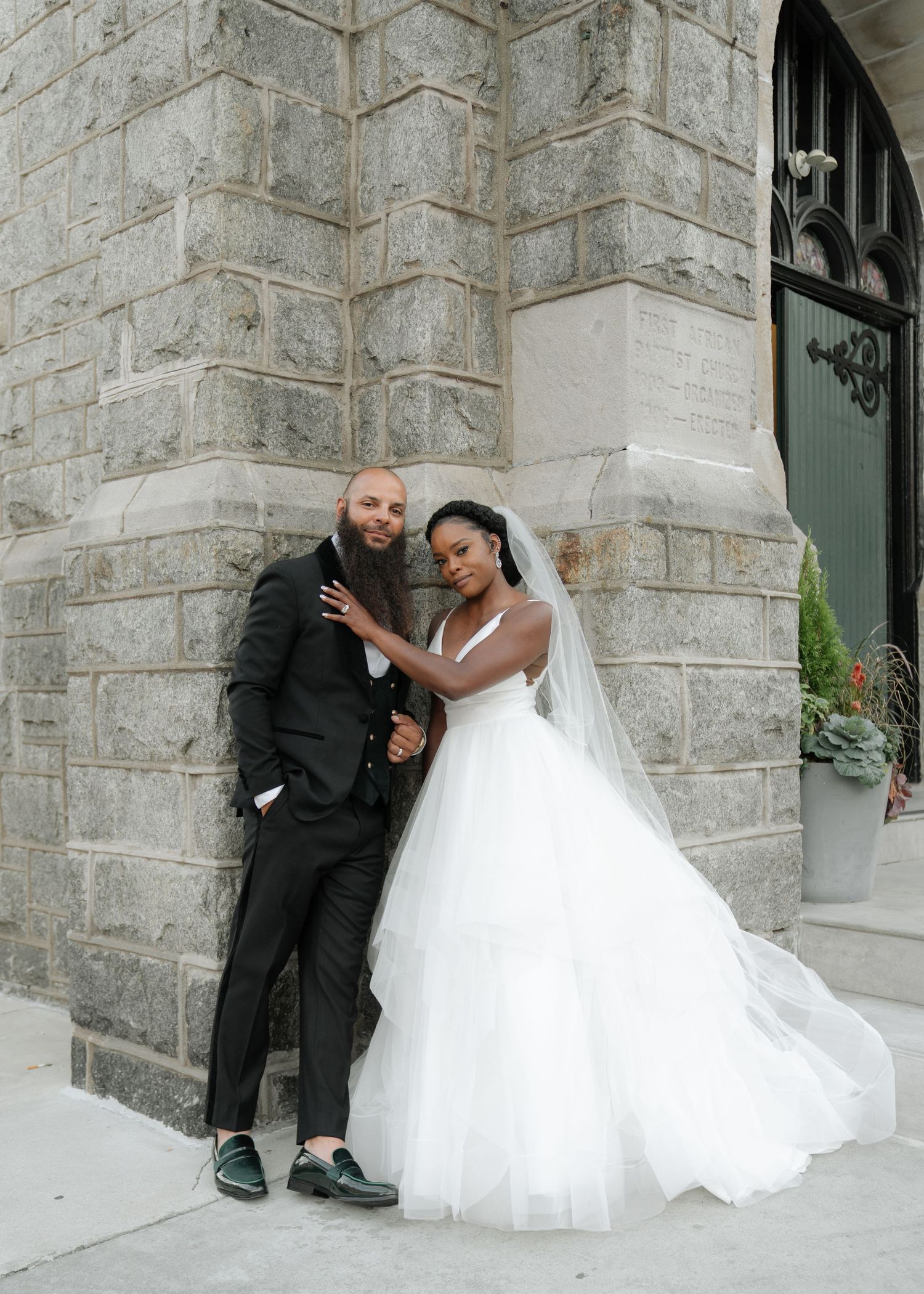 A couple poses against a stone church wall for romantic wedding portraits.