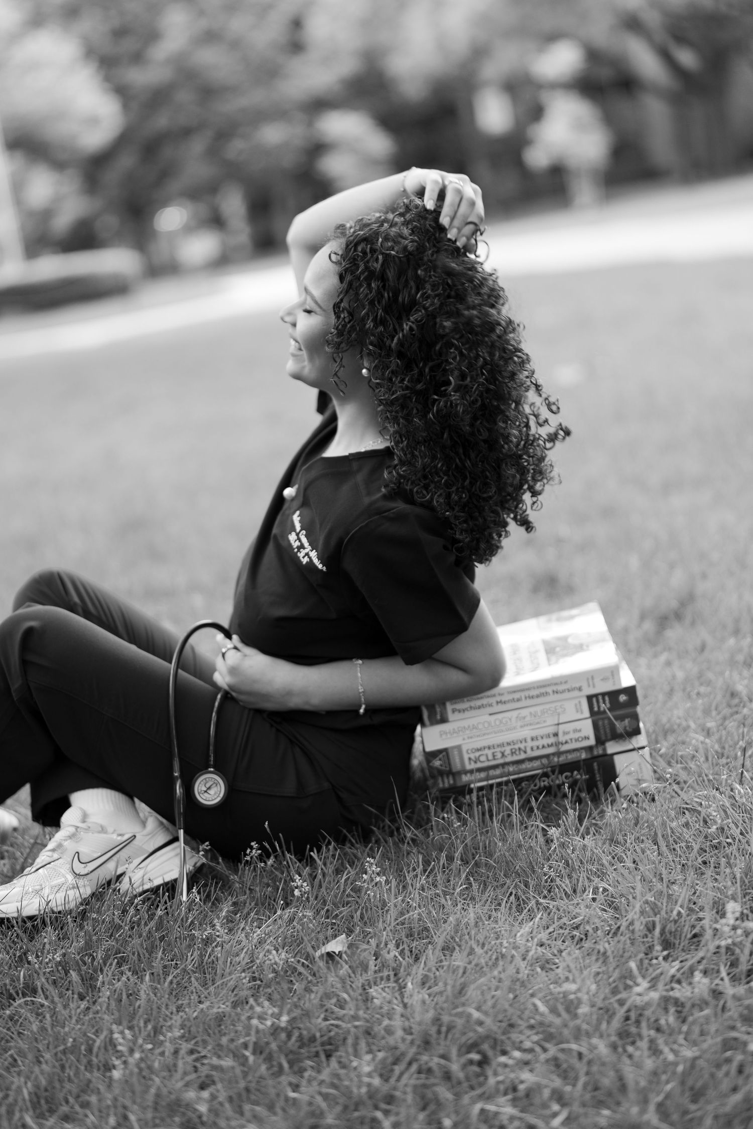 Black and white photo of curly-haired nursing student sitting on grass with books.