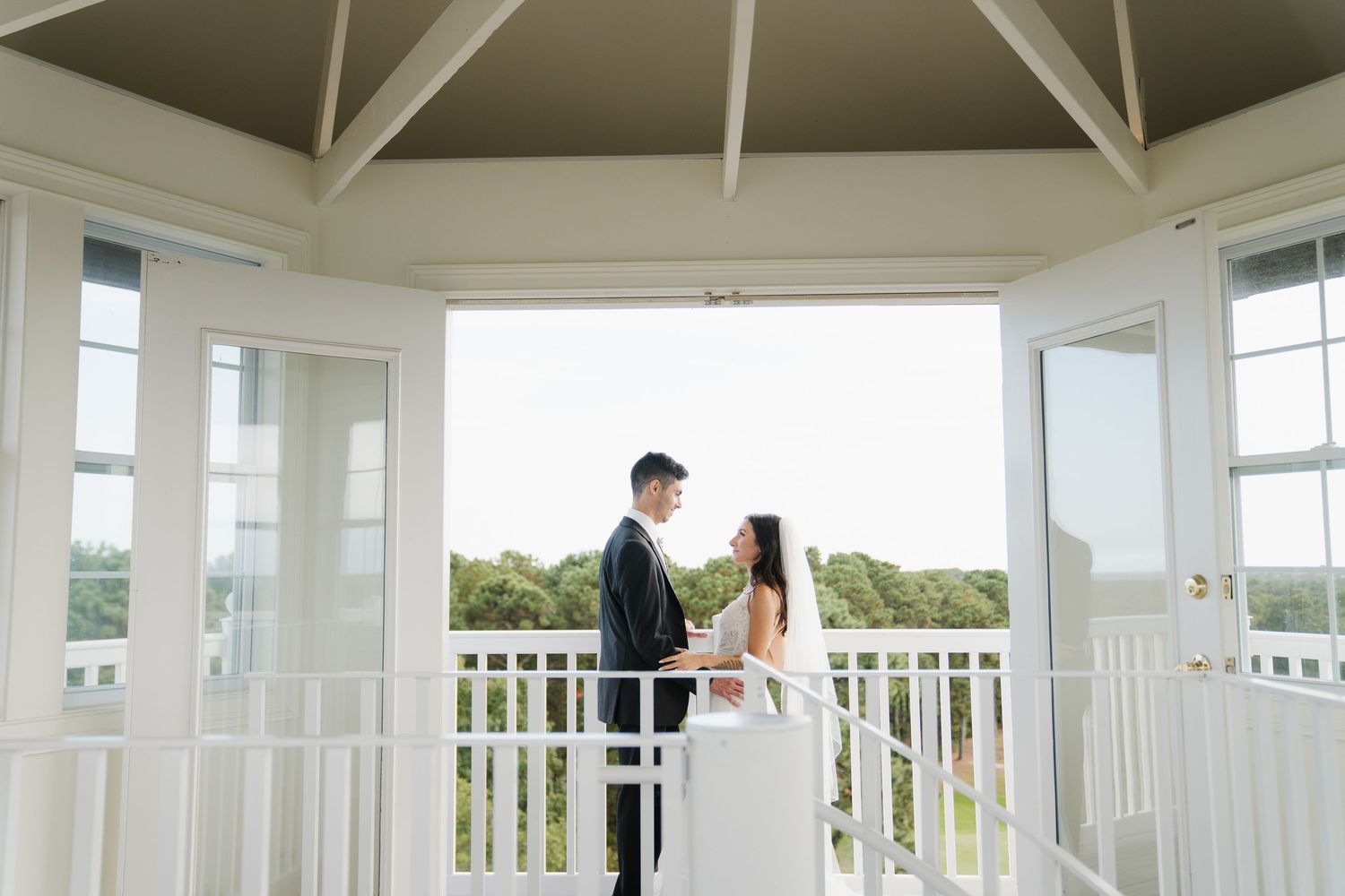 A couple shares a romantic moment on a white wraparound porch overlooking a coastal landscape.