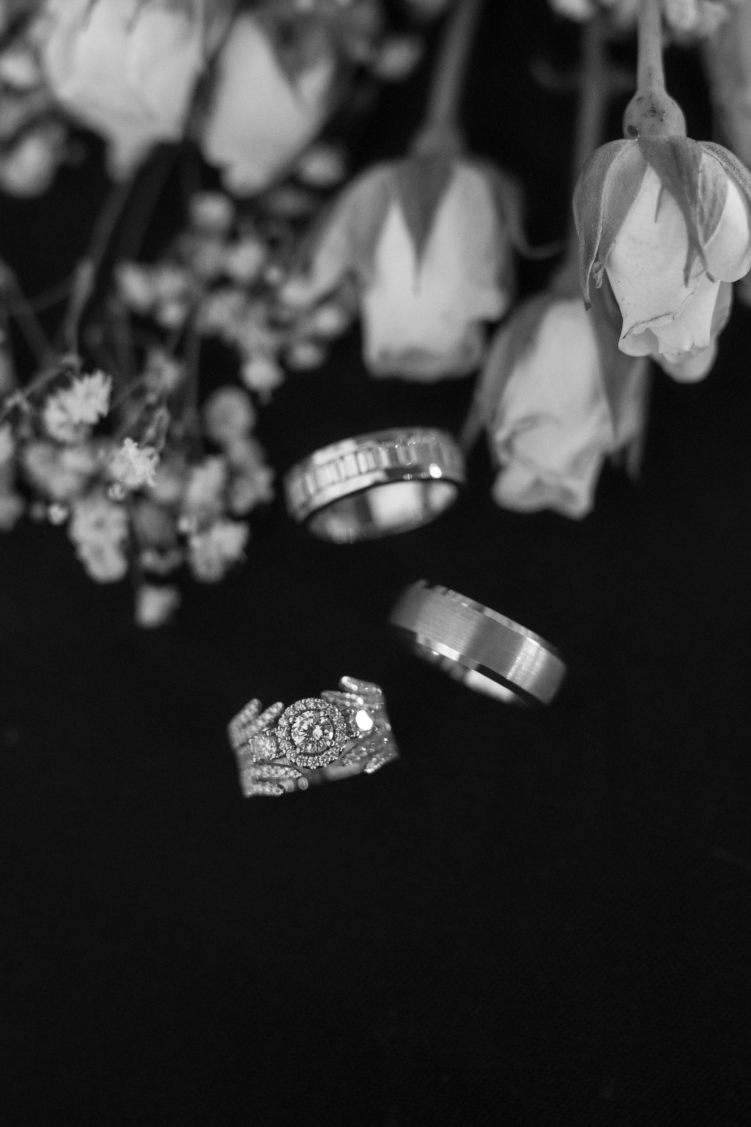Black and white photo of wedding rings with delicate white flowers in soft focus.