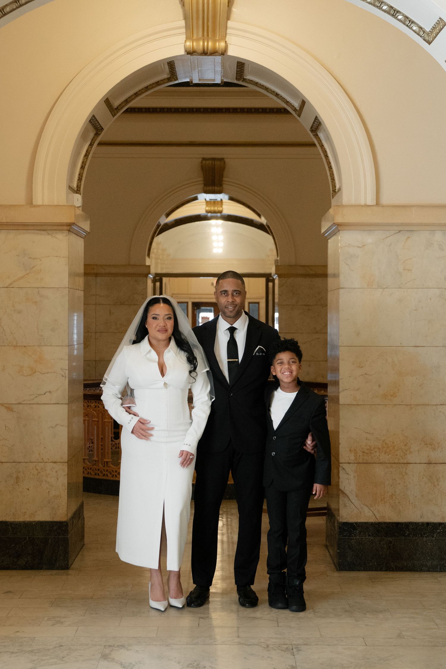 People in formal attire pose beneath elegant marble arches in a grand hallway.