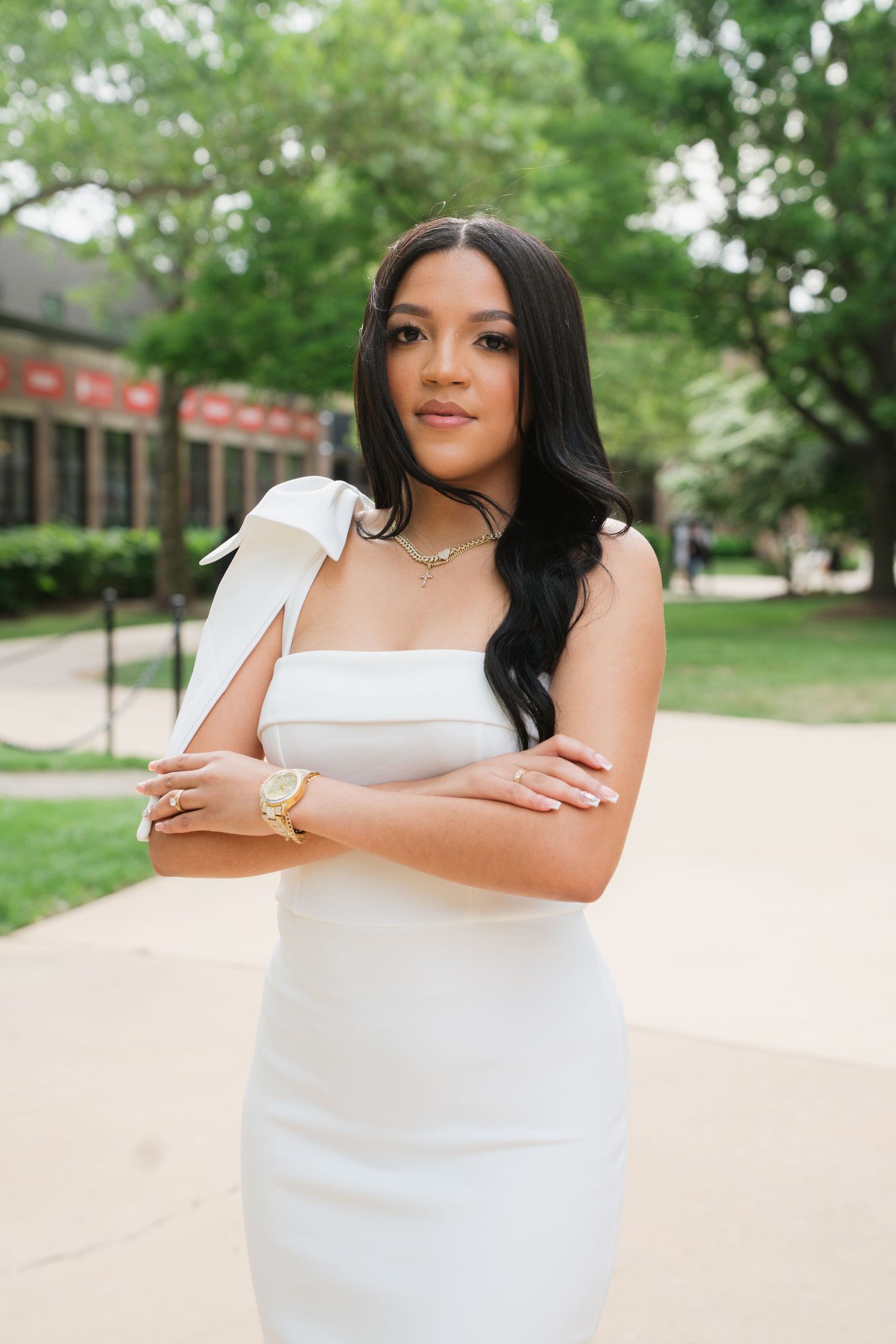 Graduate posing in white dress against outdoor campus background.