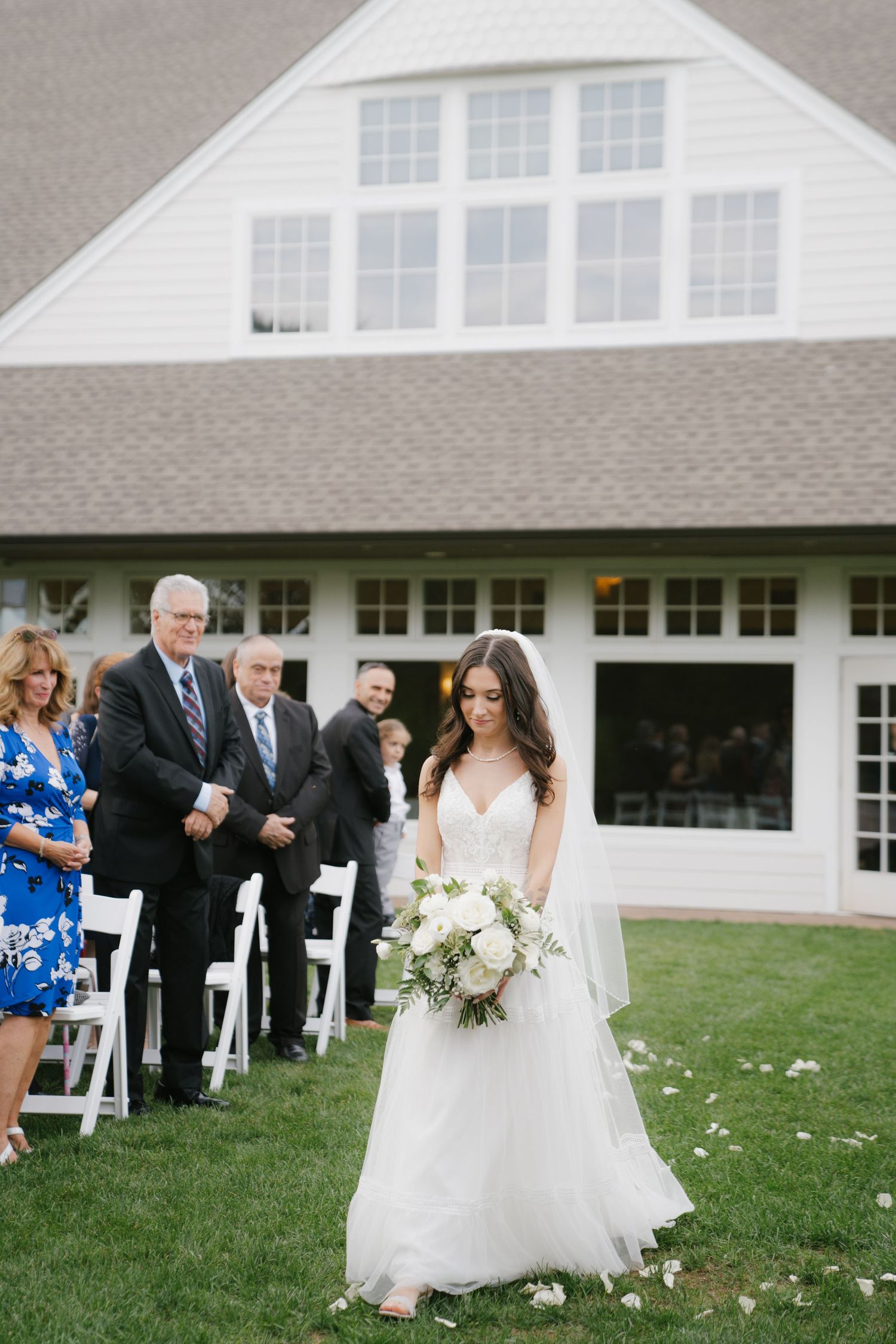 A wedding ceremony setup on a lawn with white chairs in front of a white building with guests gathering around.