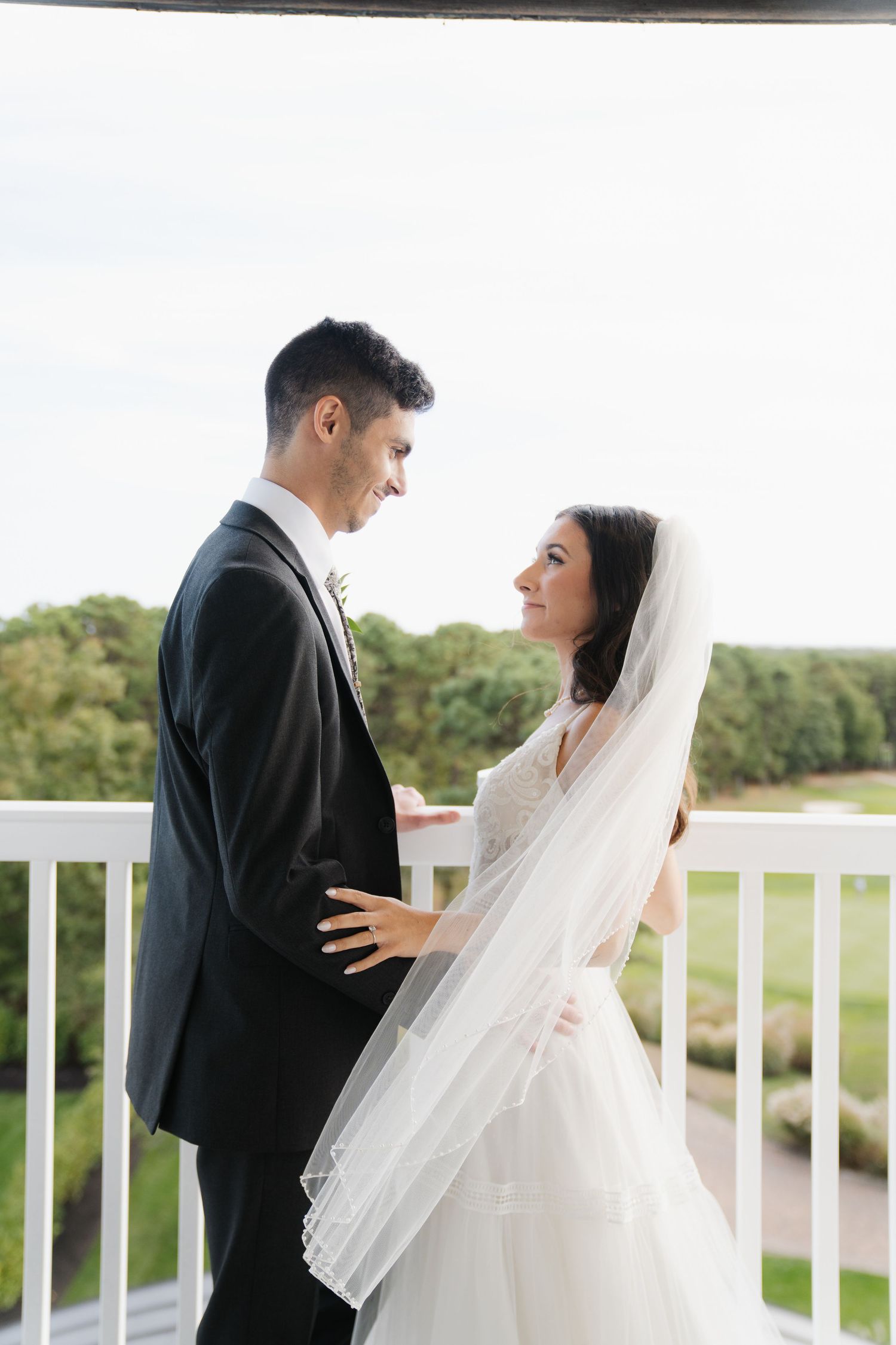 Romantic wedding couple shares intimate moments on a white balcony overlooking a scenic landscape.
