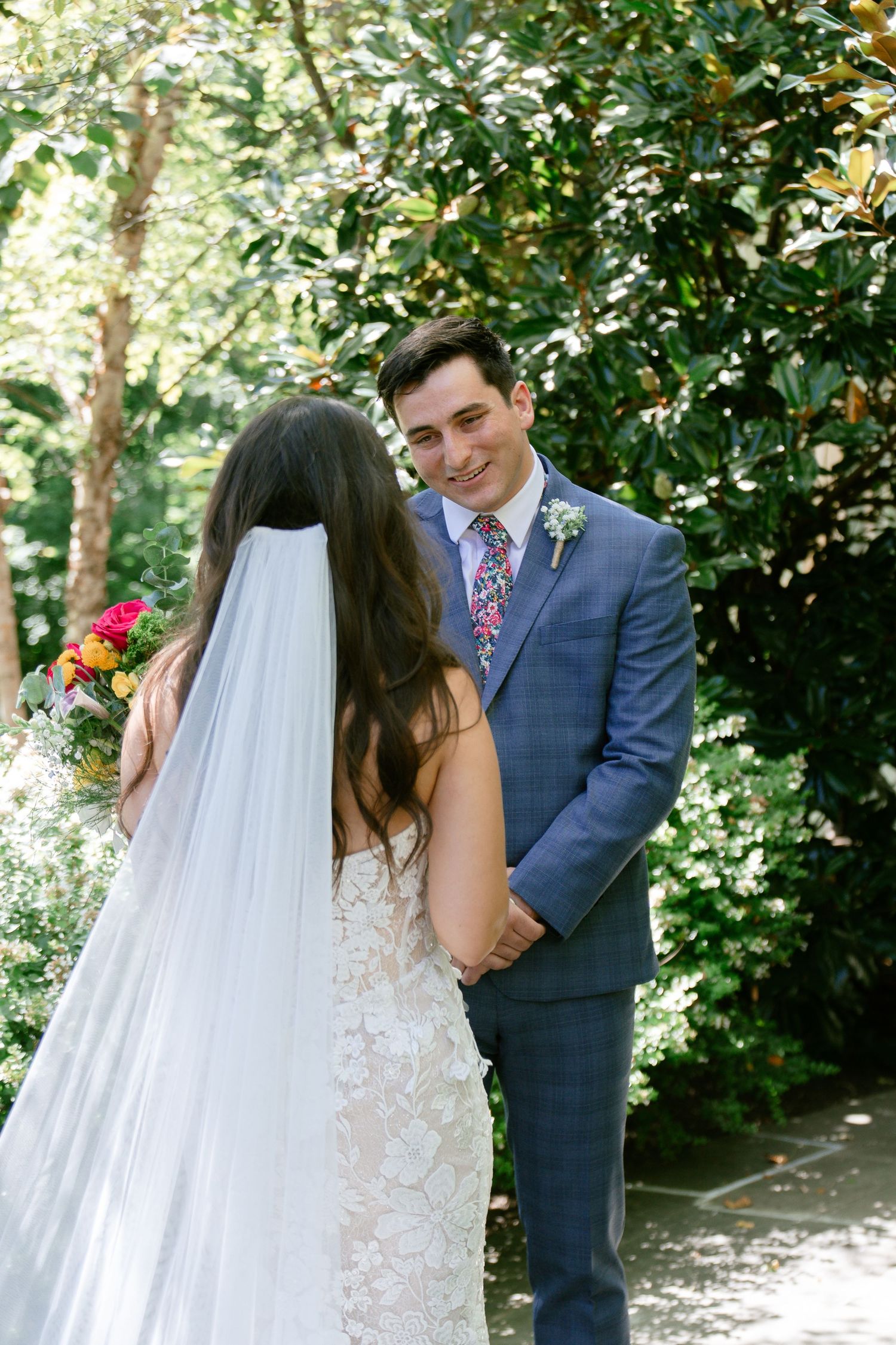 Romantic first look sequence between newlyweds in a garden setting with white floral decorations.