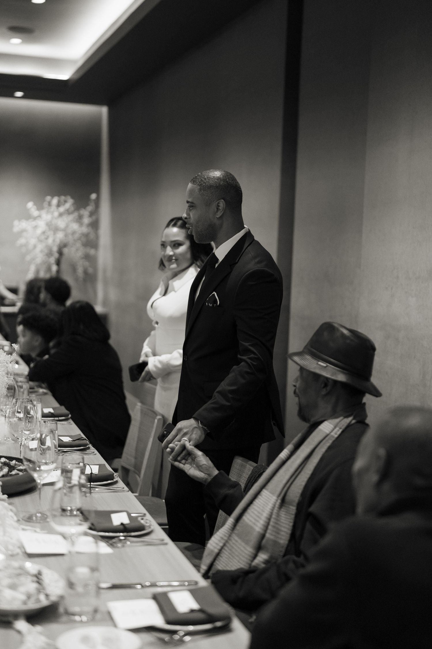 Wedding reception guests standing at an elegant dining table in formal attire.