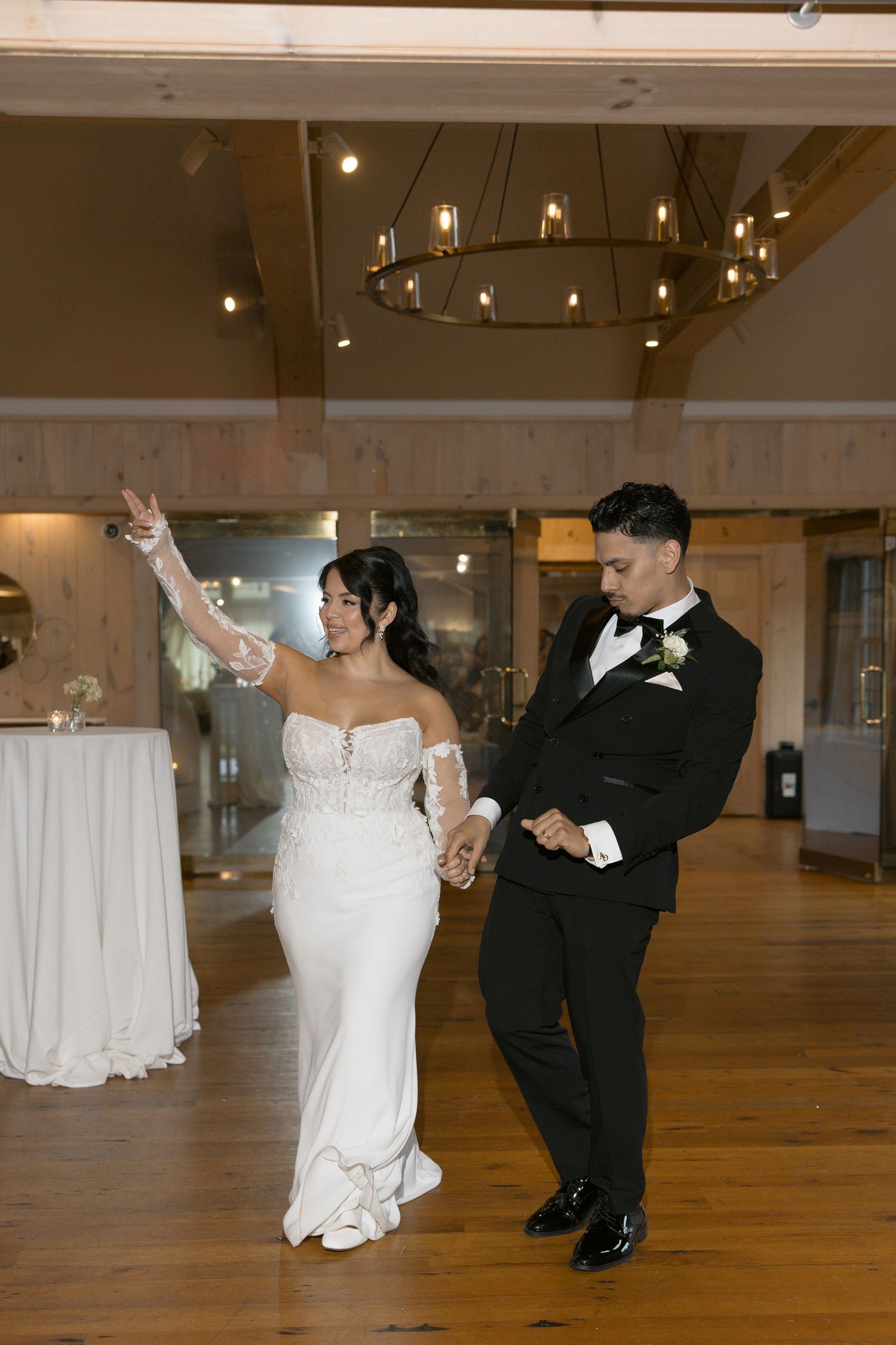 Bride in white lace gown and groom in black tuxedo share their first dance in an elegant wedding reception.