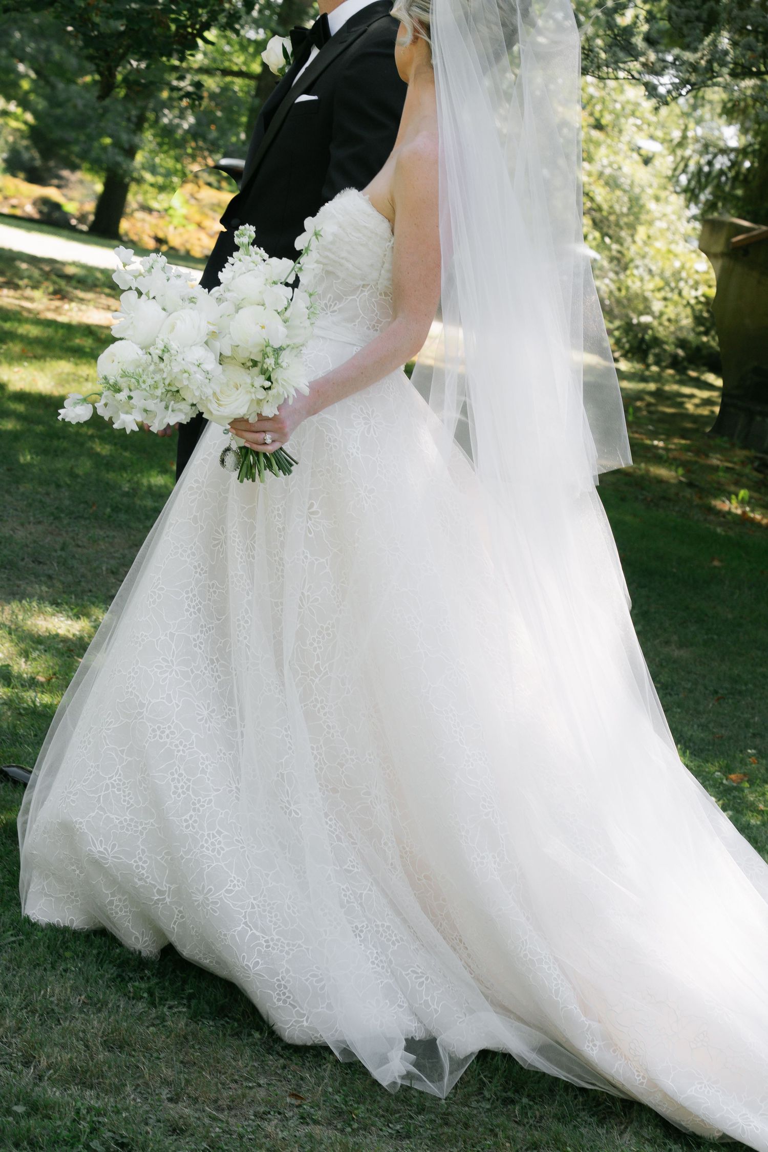 Close-up details of a flowing white wedding dress and bouquet in an outdoor garden setting.