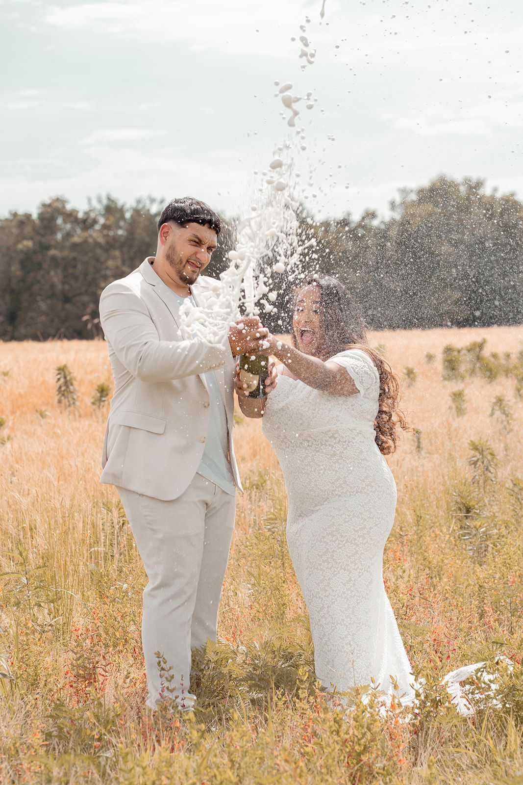A couple celebrates with champagne in a golden field during sunset.