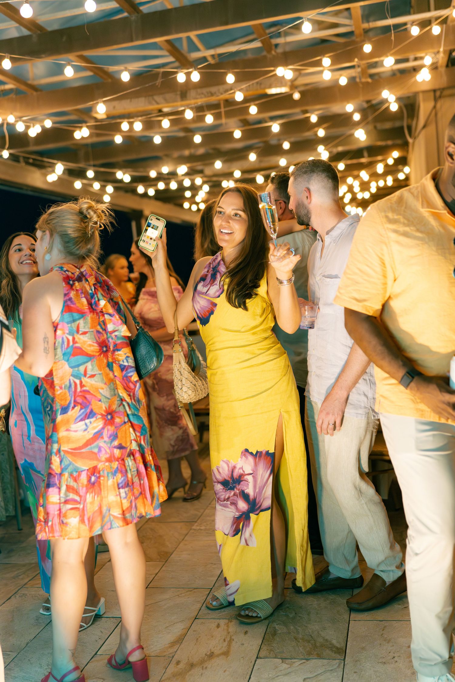 Wedding guests dance and celebrate under twinkling string lights at an outdoor reception venue.