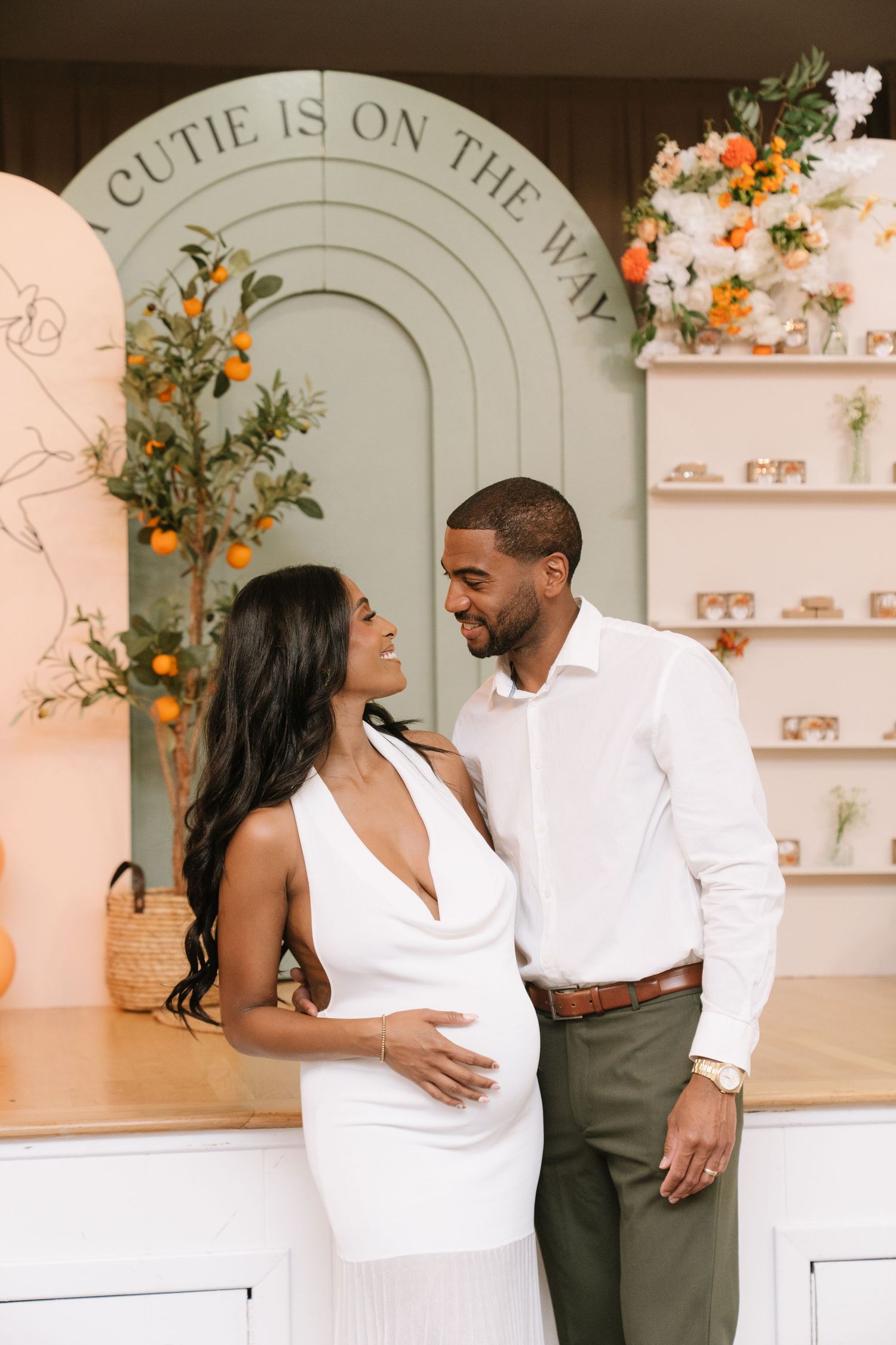 Romantic couple in white and grey outfits posing against mint green arch backdrop.