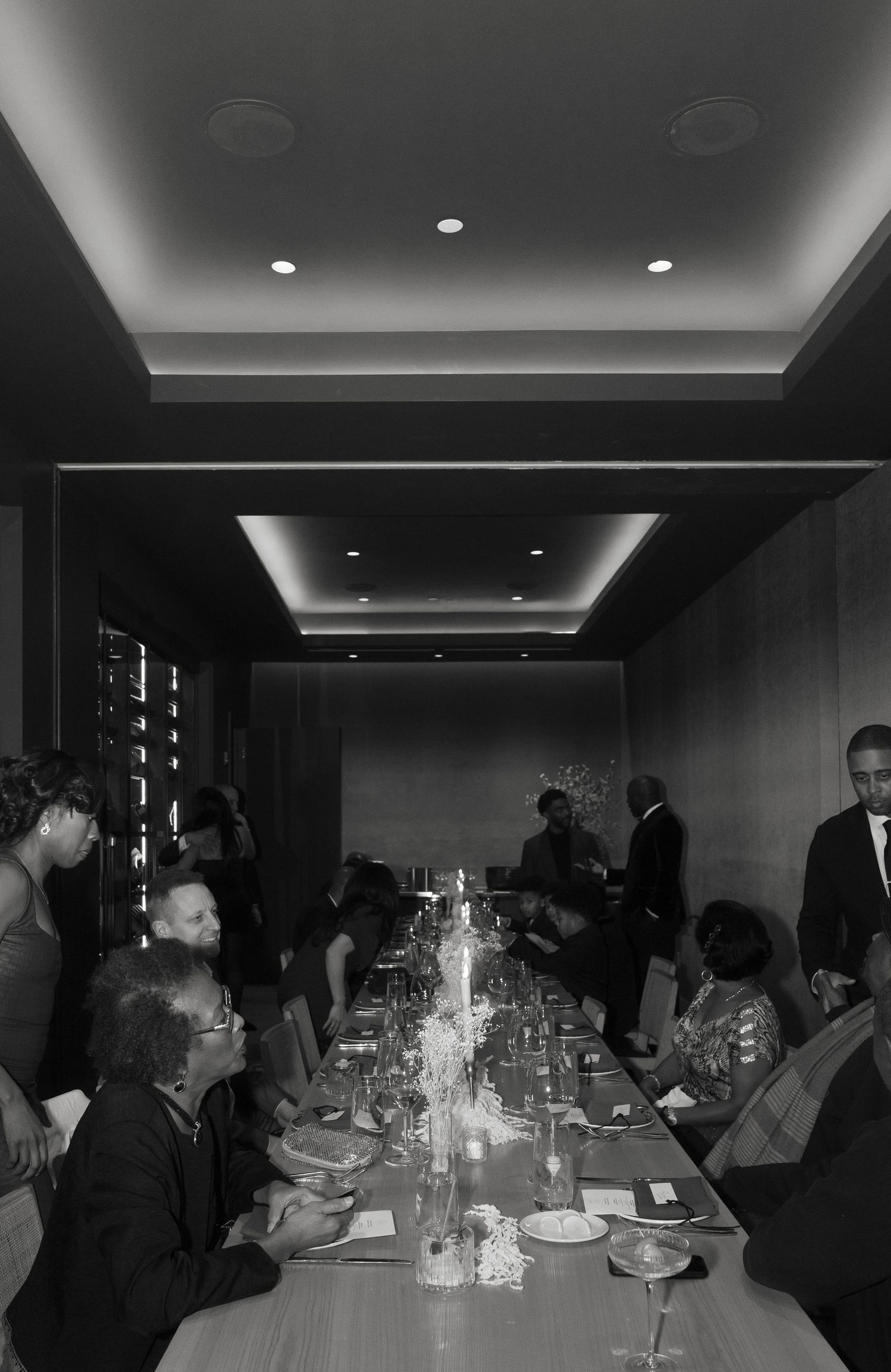 A dimly lit wedding reception dinner table with guests seated in a modern venue.