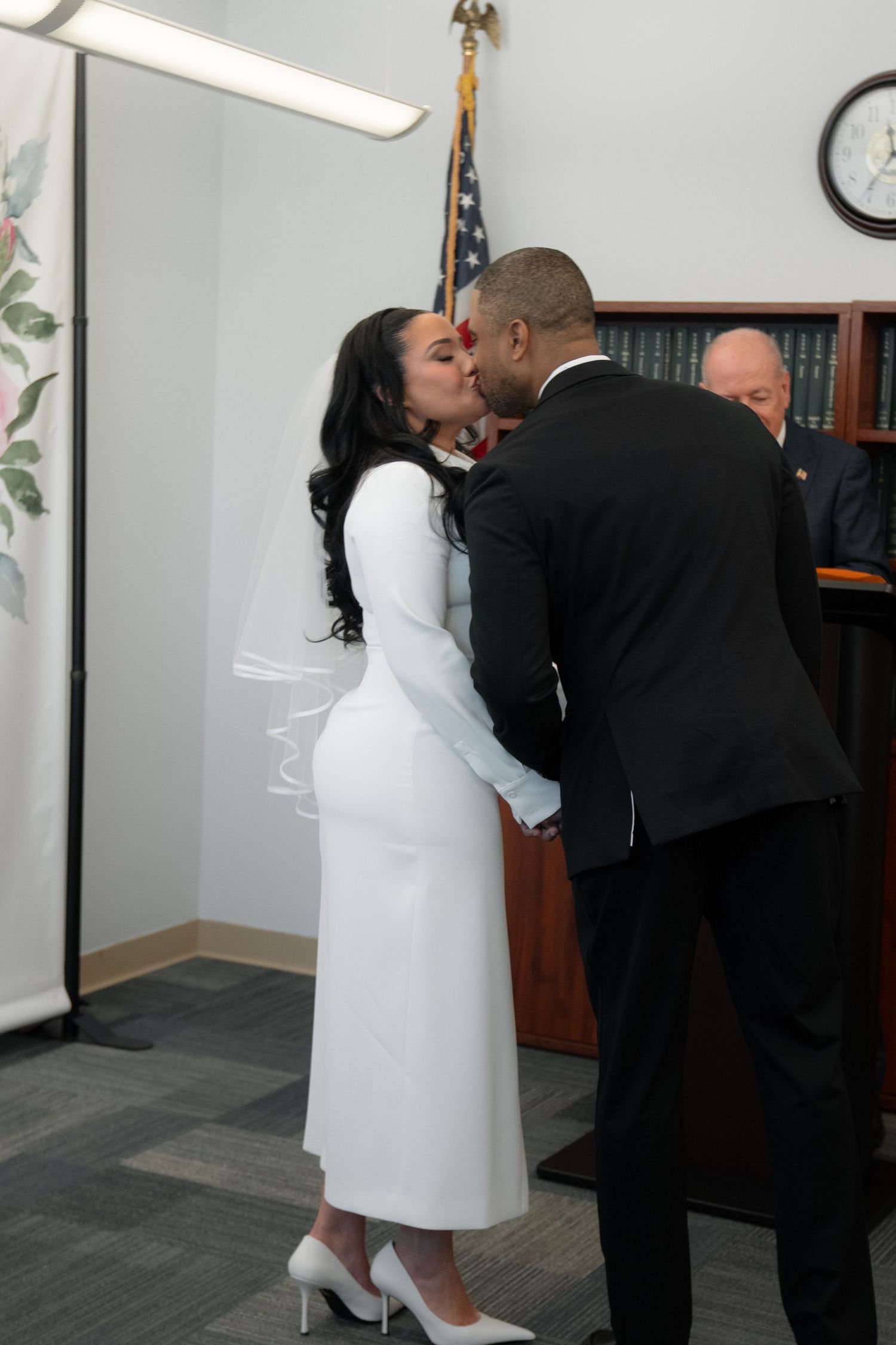 A couple shares an intimate moment in formal attire at what appears to be a courthouse or official building.