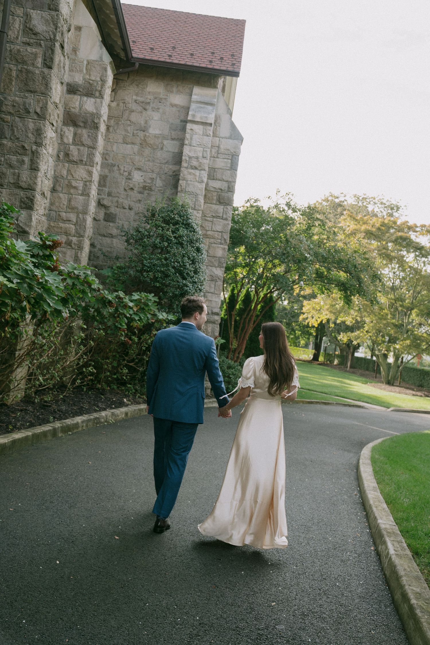 A couple walks along a curved pathway outside a stone church on an autumn evening.