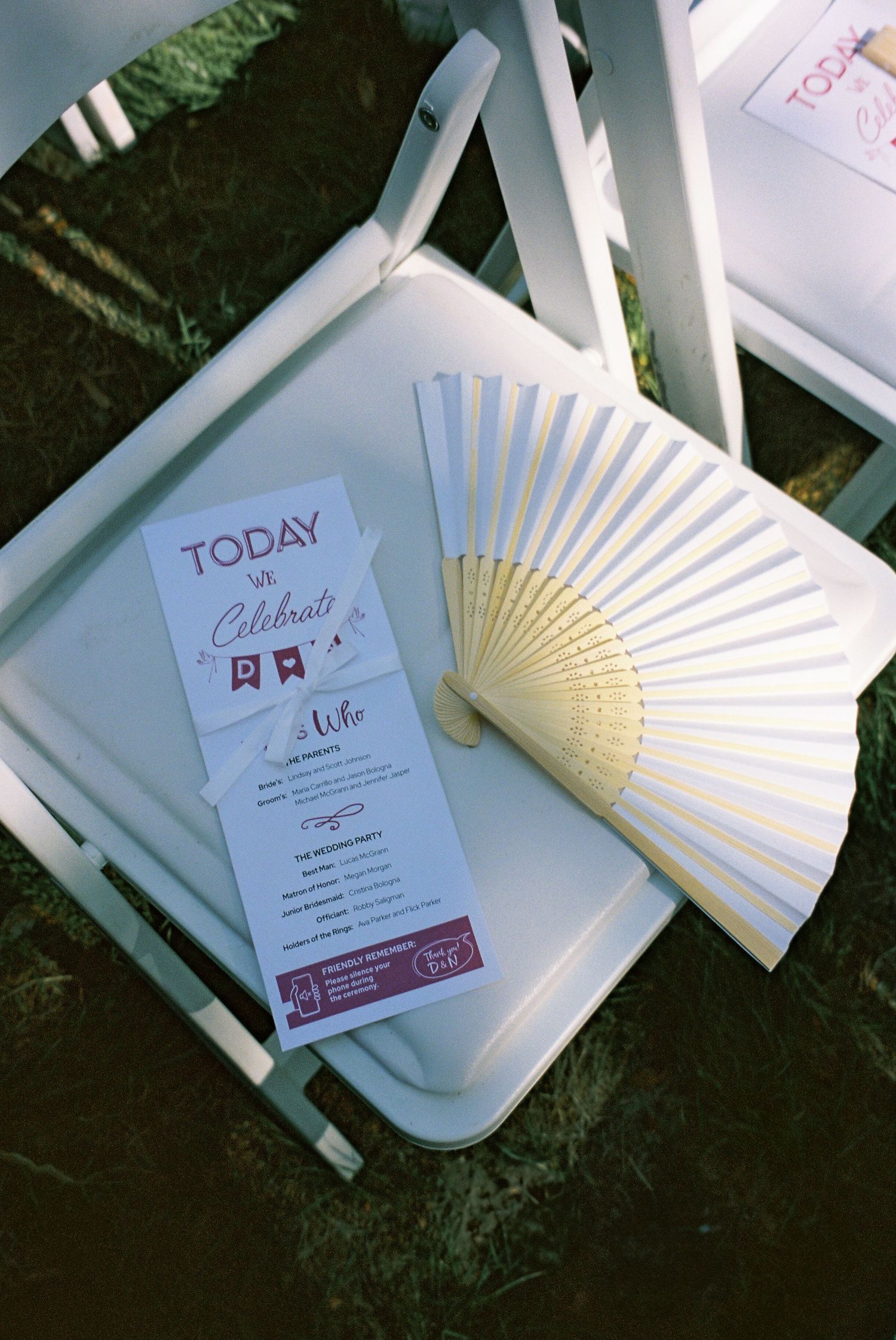 Wedding ceremony programs and decorative paper fans arranged on white chairs.