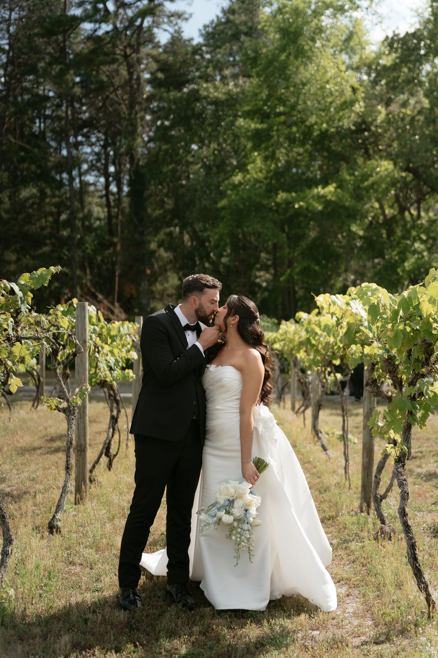 Bride and groom share a romantic kiss among lush vineyard rows on their wedding day.