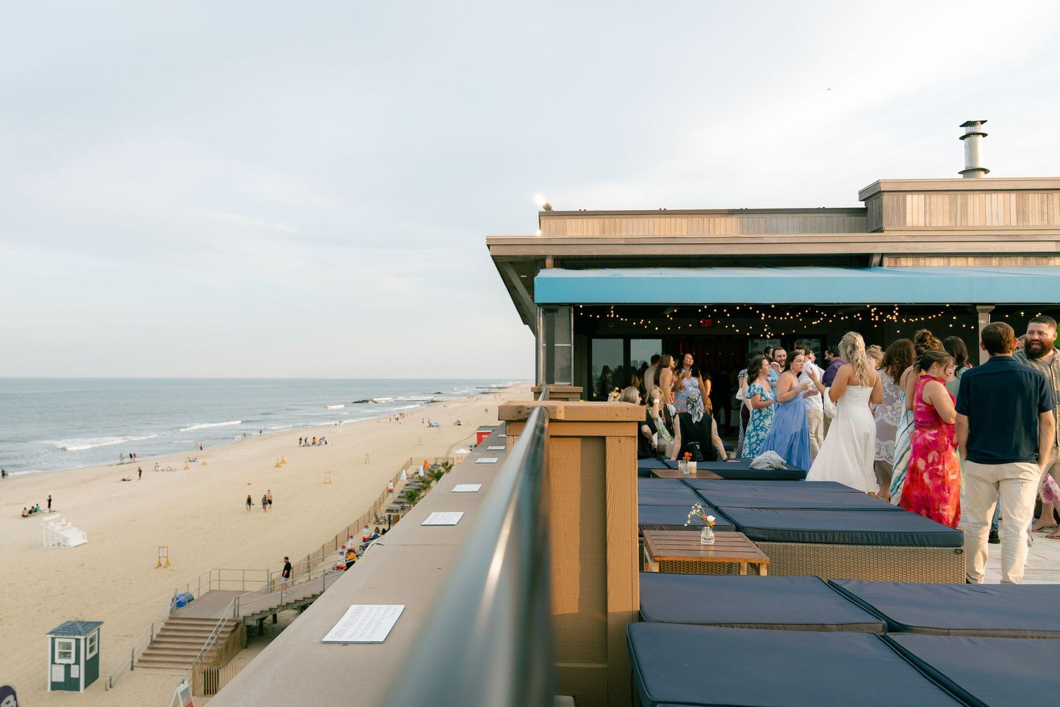 People gather on a rooftop deck overlooking a beach with ocean views.