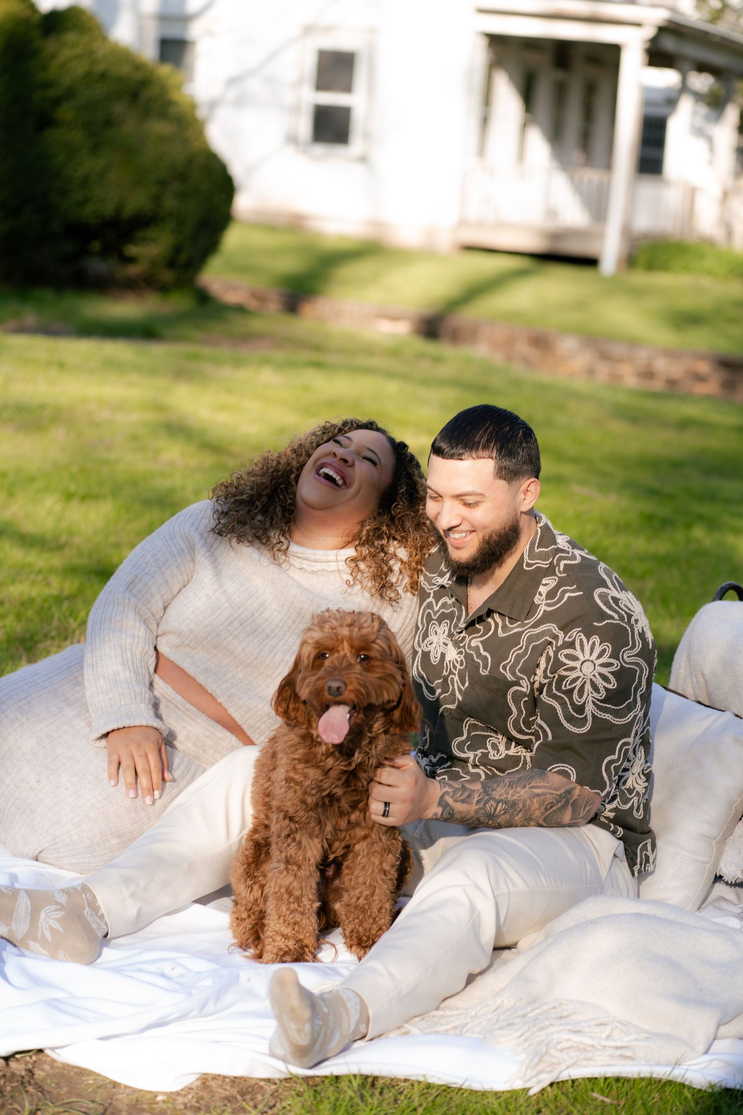 Couple lounging on white blanket outdoors with their brown poodle.