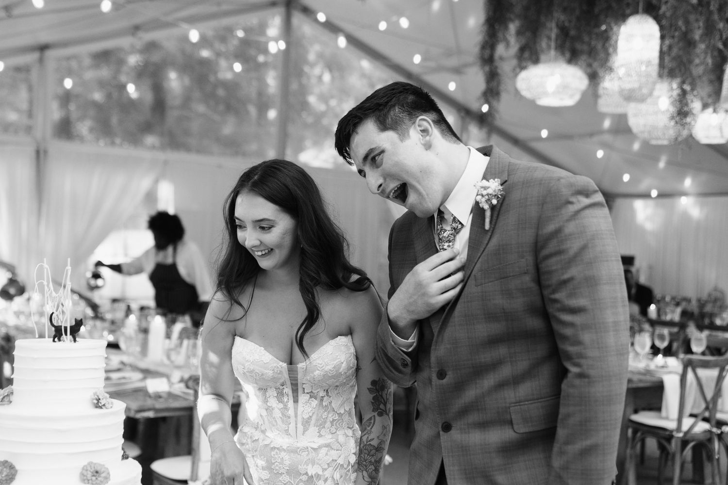 A happy couple shares a joyful moment at their wedding reception under twinkling lights in a tent.